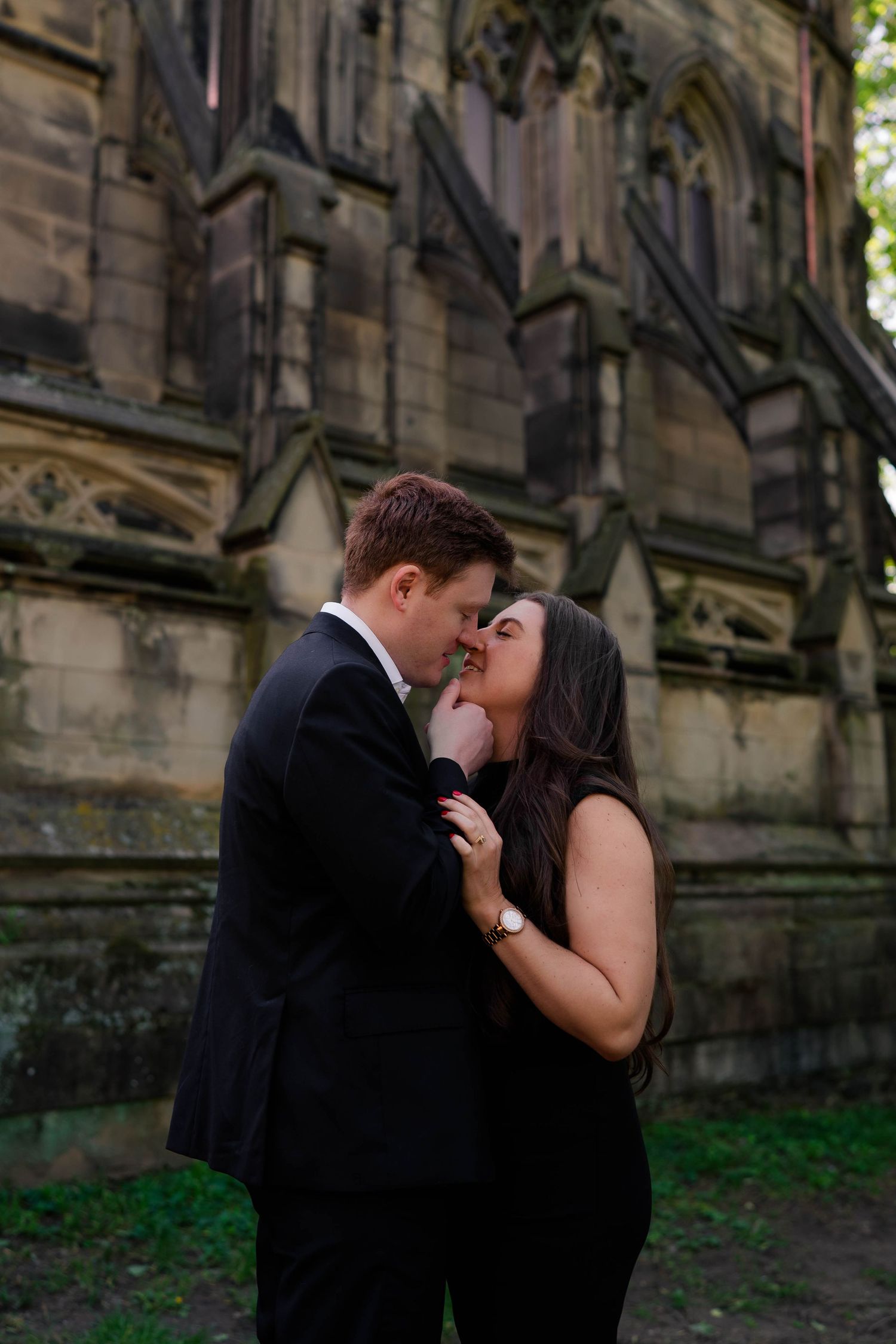 Couple sharing an intimate moment about to kiss in front of a historic stone church.