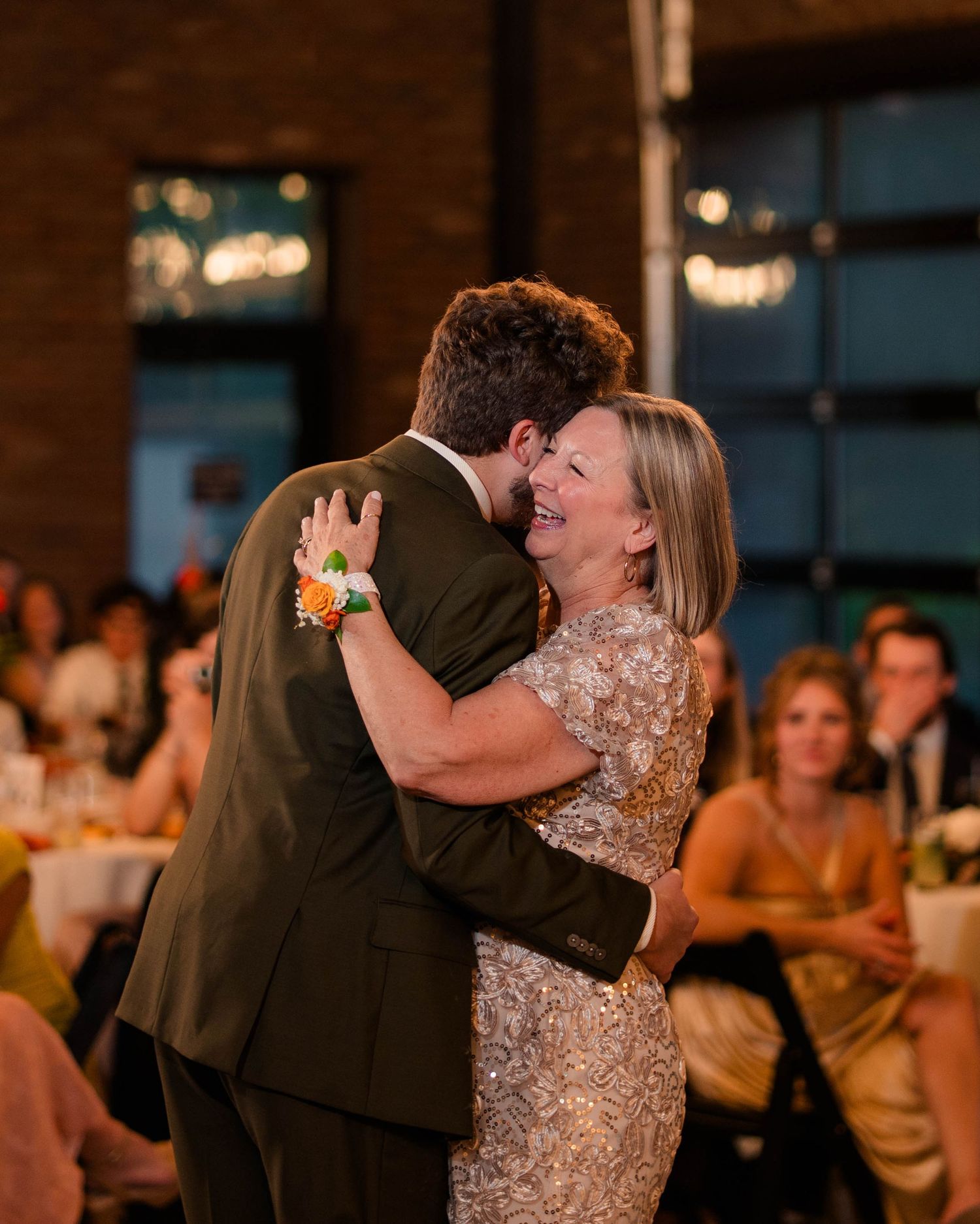 Groom in olive suit shares emotional mother-son dance at wedding reception.