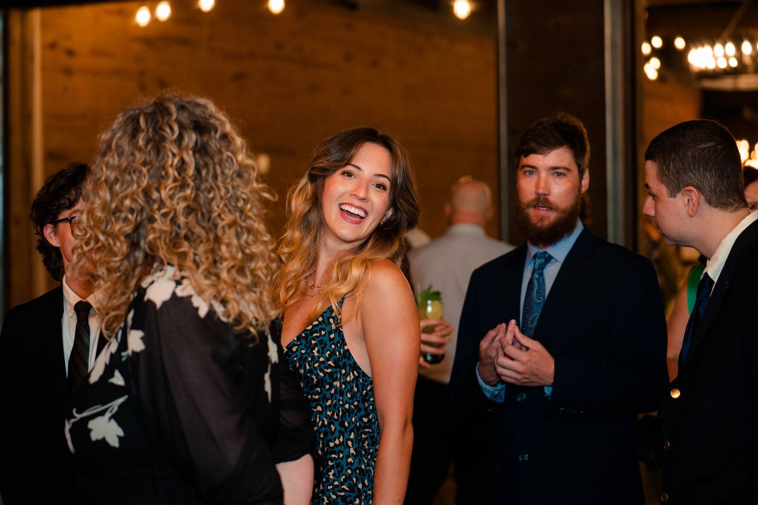 Guests laughing and socializing at a wedding reception in a warmly lit venue.