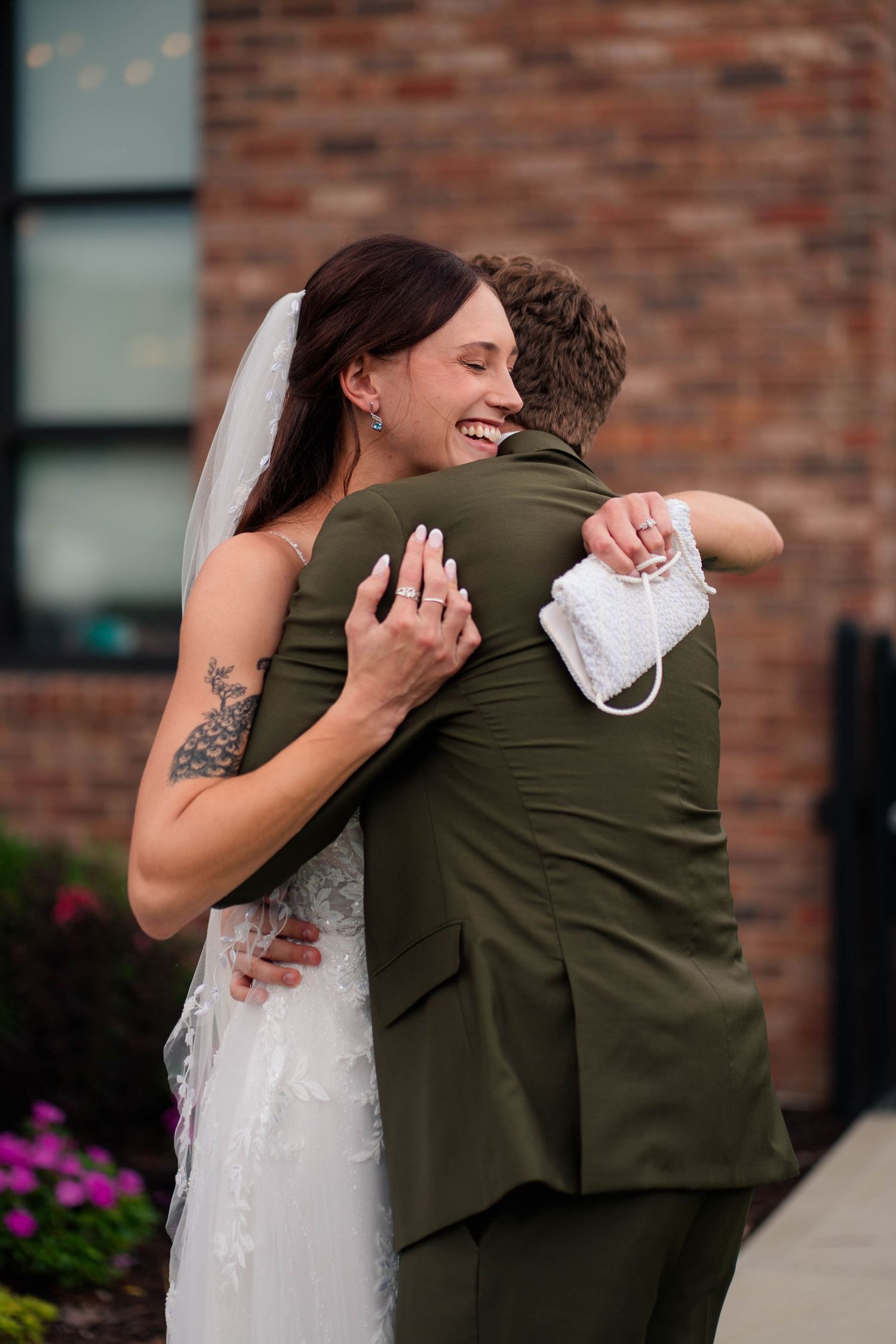 Bride in white gown and veil embraces groom in olive suit during first look.