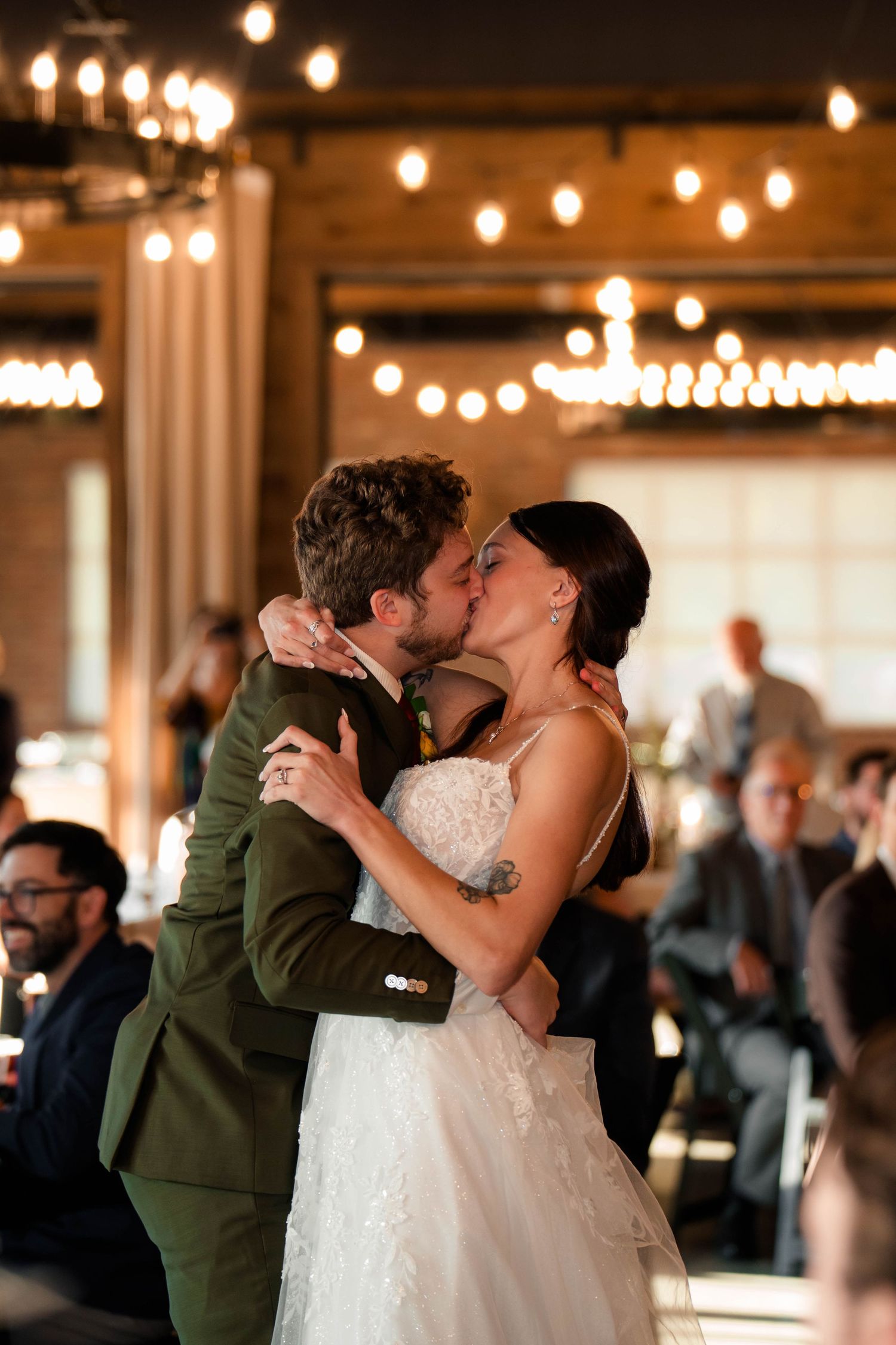 Bride and groom share a romantic kiss on the dance floor surrounded by Edison bulb string lights.
