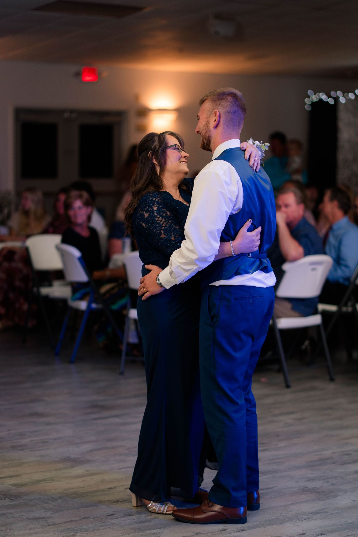 Mother and groom share an emotional mother-son dance at wedding reception in softly lit venue.