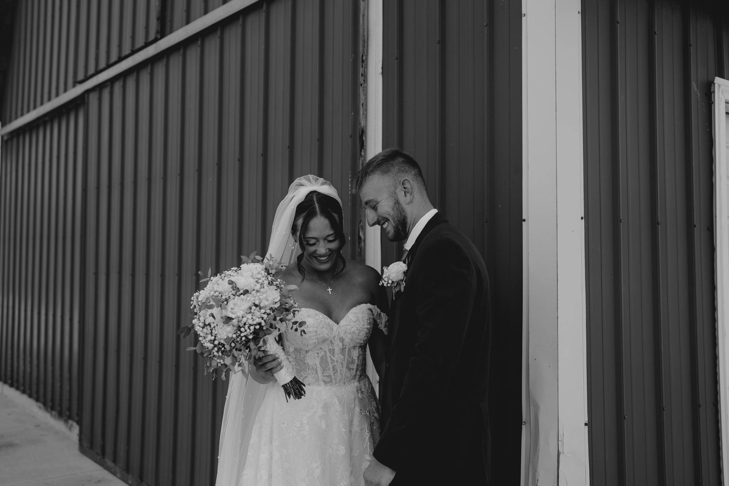 Black and white photo of a bride and groom sharing a tender moment outside a barn on their wedding day.