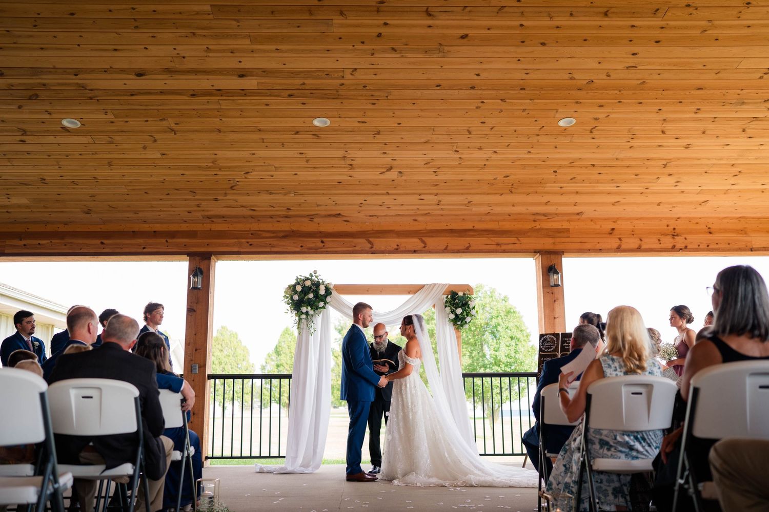 Bride and groom exchange vows under floral arch at outdoor wedding ceremony.