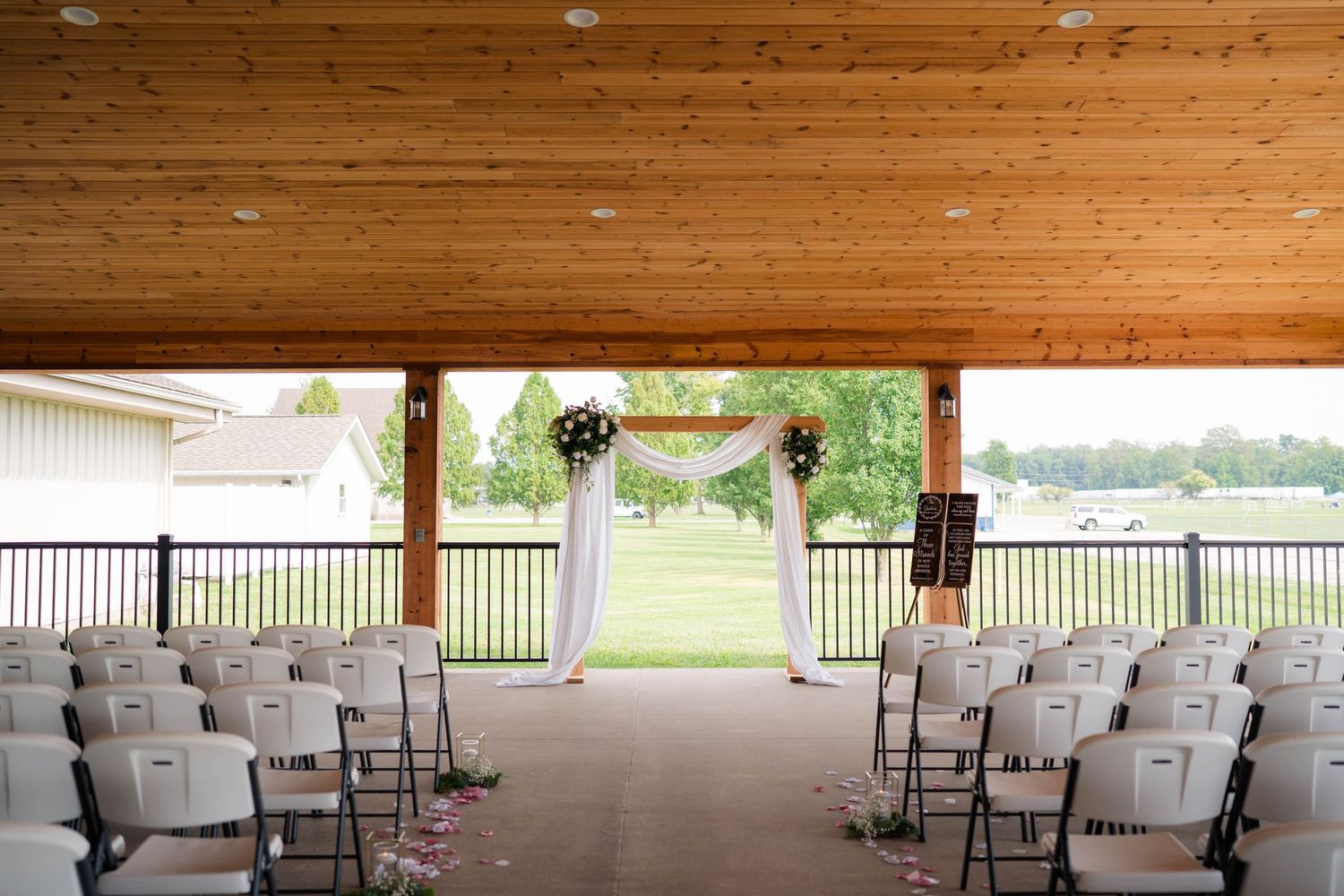 Elegant outdoor wedding ceremony setup with white chairs, floral arch, and scenic green landscape view.