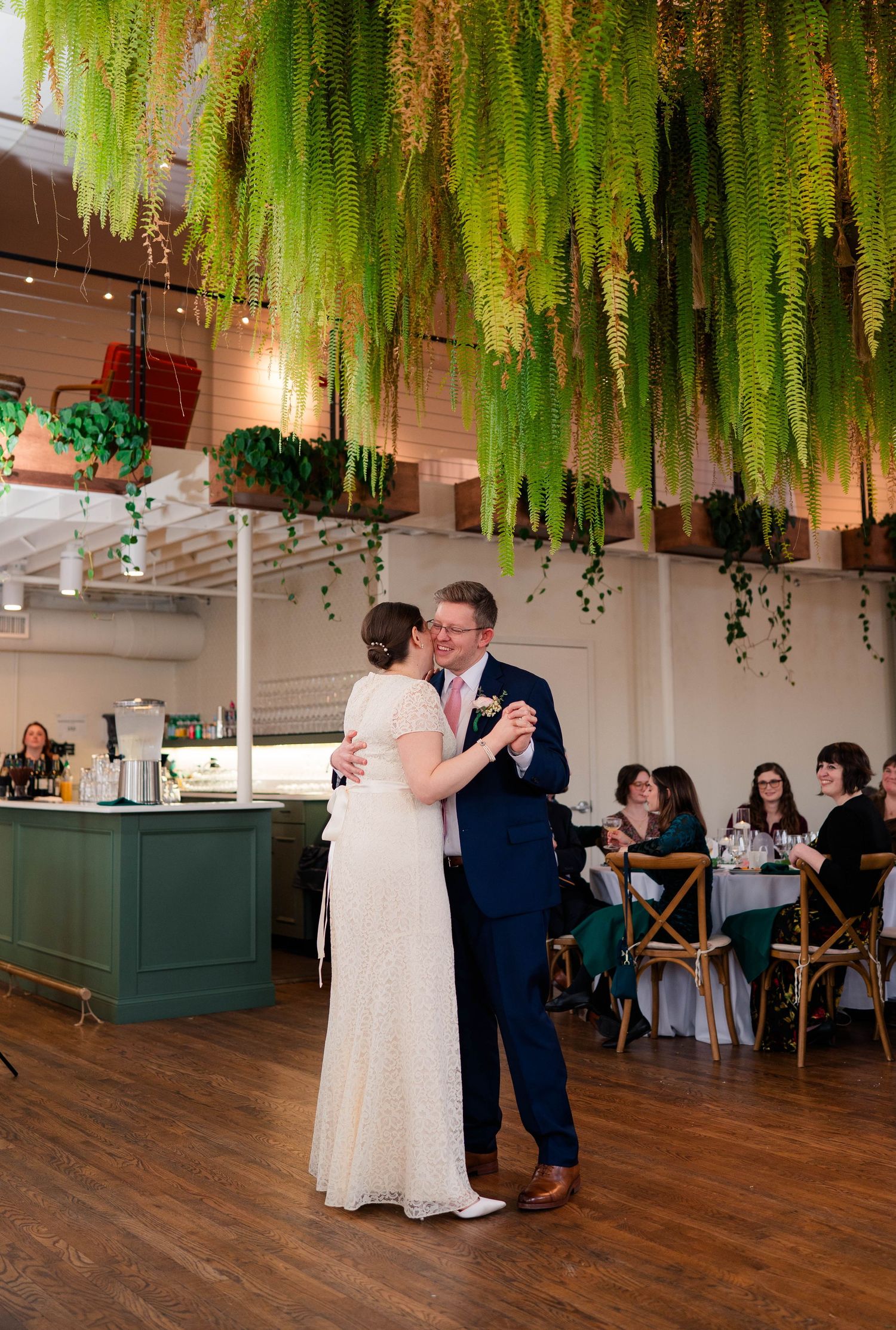 Bride and groom kissing under hanging fern installation during first dance at reception.