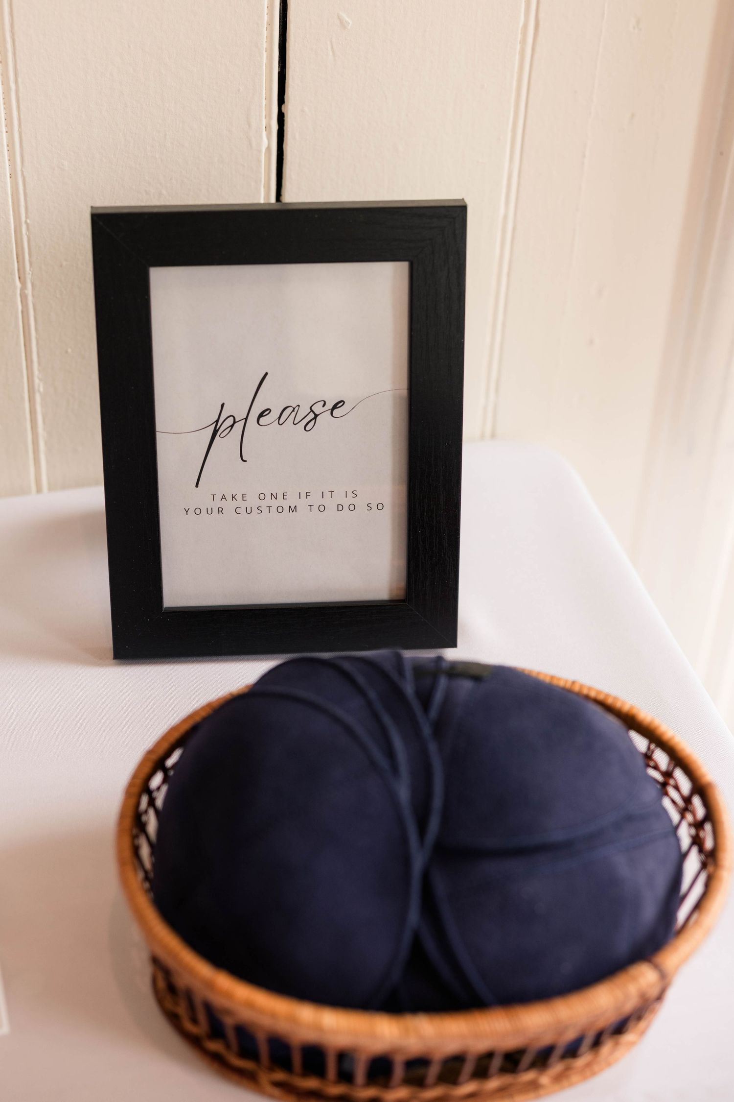 Framed sign reading please take one if it is your custom to do so beside a wicker basket of navy blue kippot.