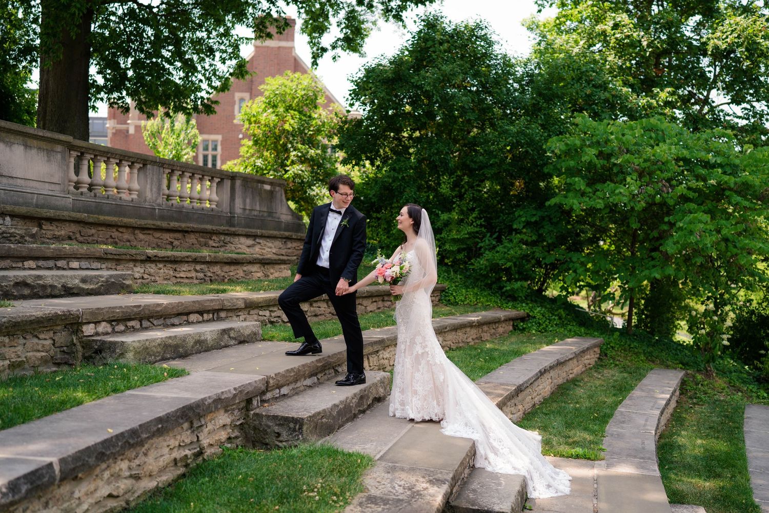 Bride and groom walking hand-in-hand on stone steps surrounded by lush greenery at elegant venue.