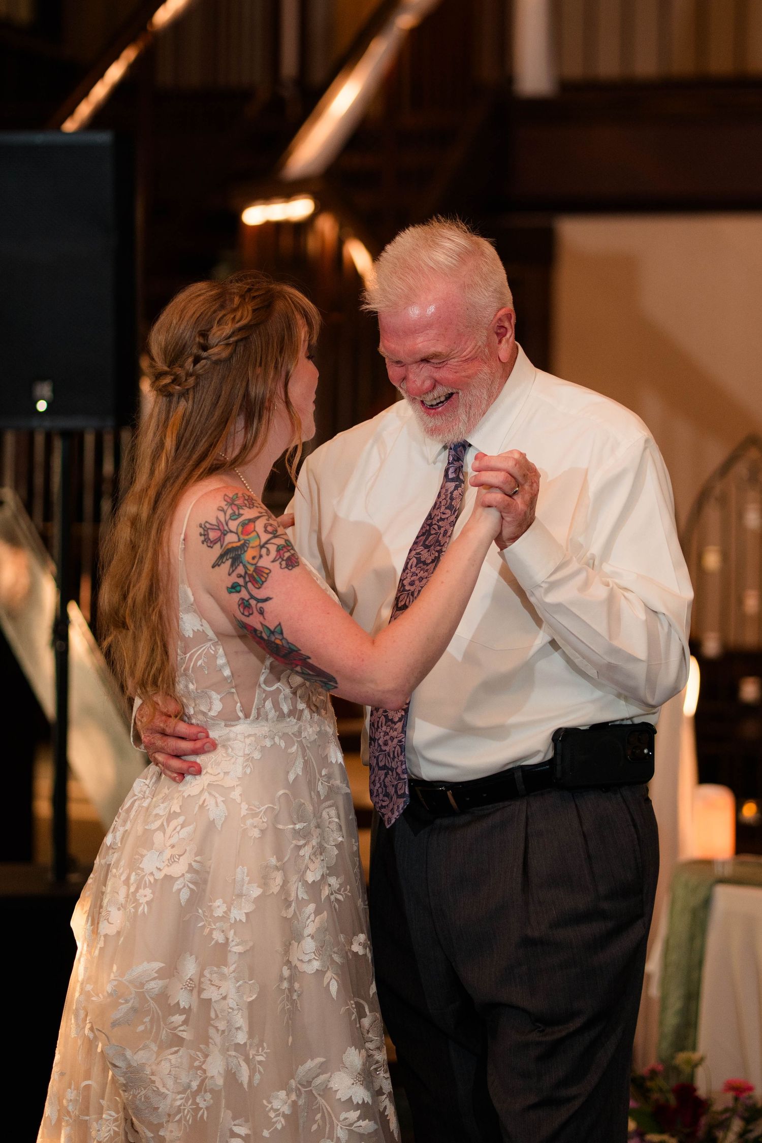 Bride with floral arm tattoo shares a joyful father-daughter dance at her wedding reception.