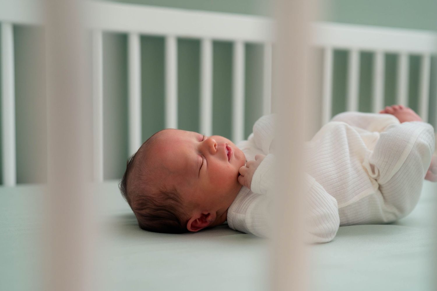 Peaceful newborn baby sleeping soundly in a white crib wearing a soft white outfit.