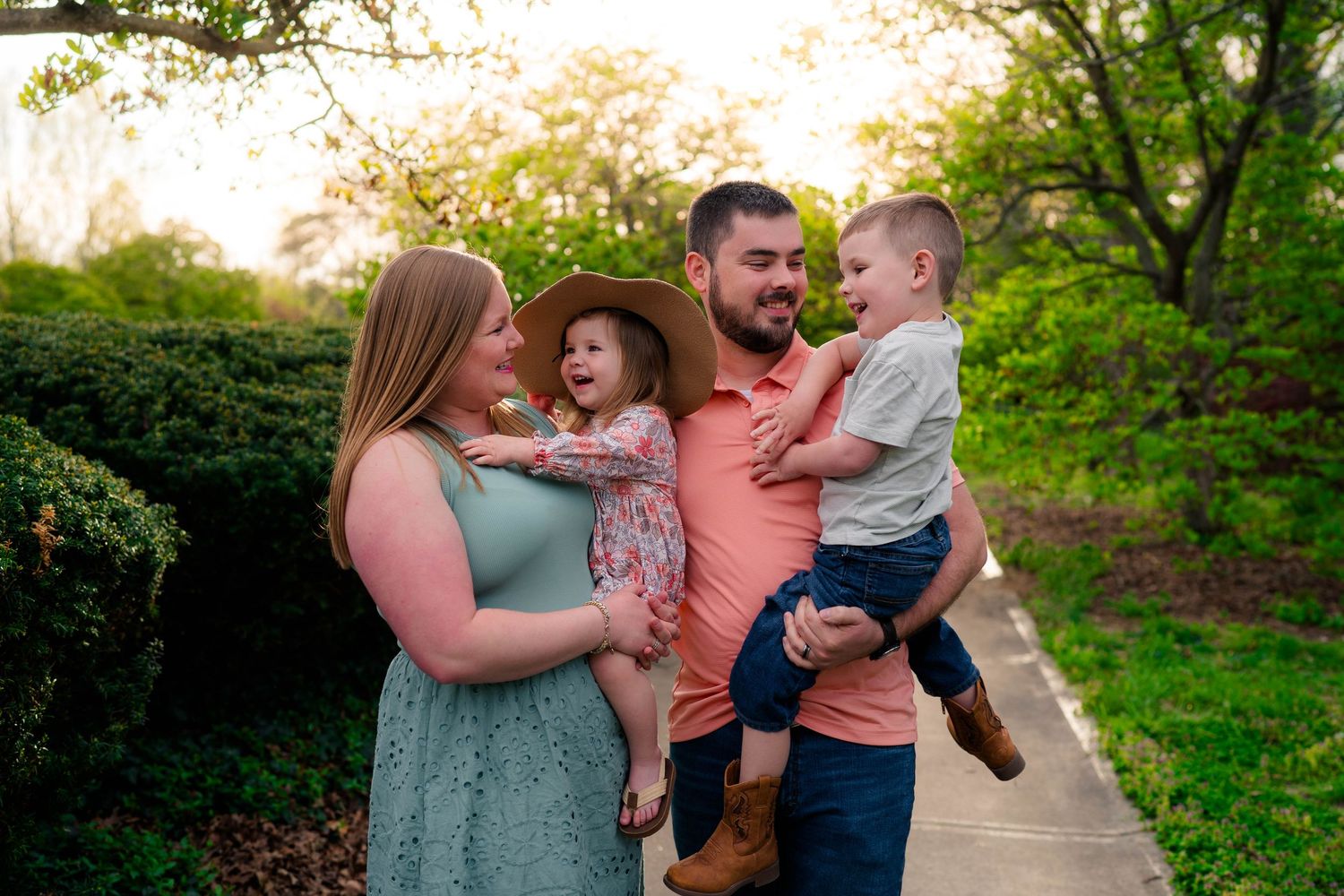 Happy family of four posing outdoors in spring garden, parents holding two young children, smiling joyfully.