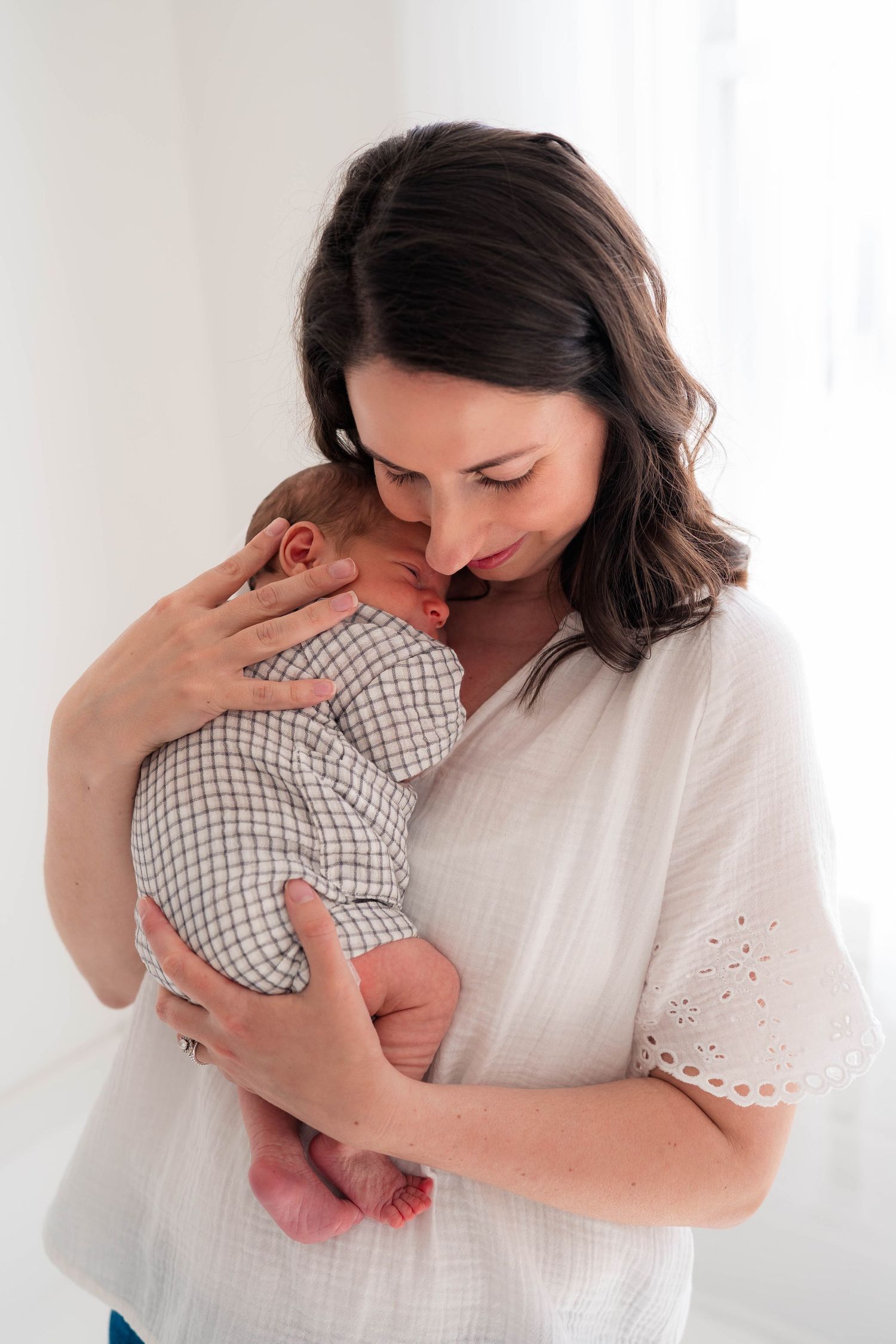 Tender moment of a dark-haired mother in a white blouse gently cradling and nuzzling her newborn.