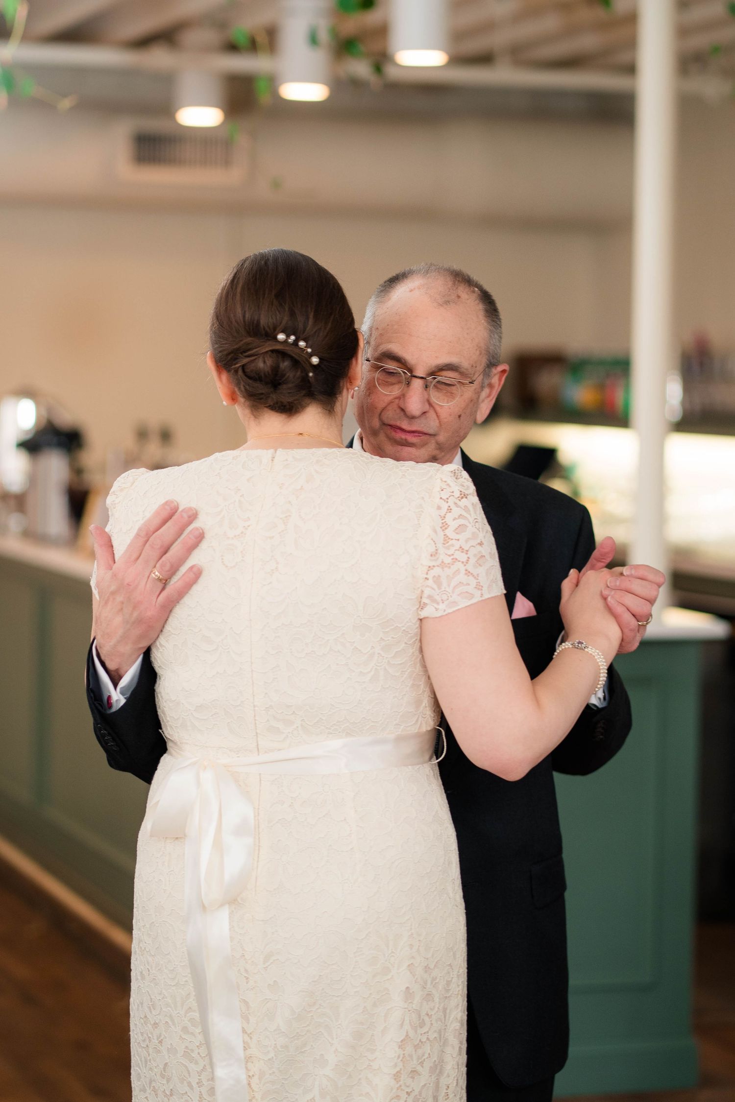 Father embracing bride in lace wedding dress during emotional father-daughter dance.