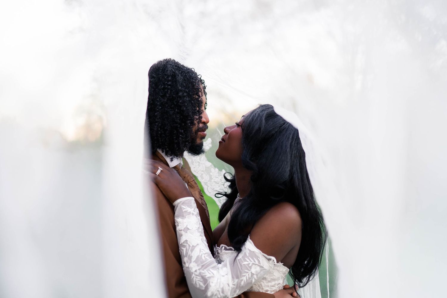 Black bride and groom share intimate almost-kiss moment wrapped in flowing white wedding veil.