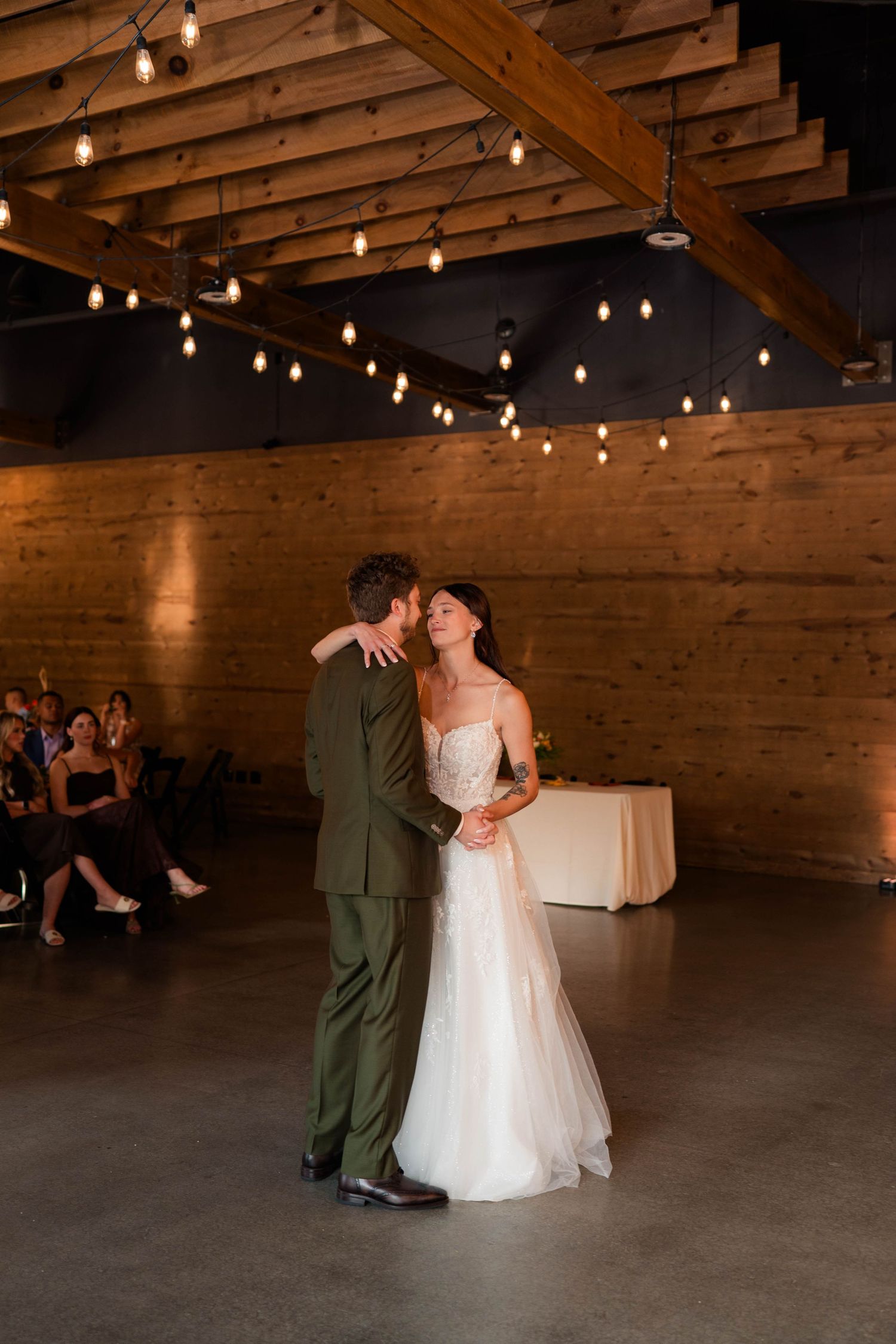 Bride and groom share first dance under warm string lights in rustic brick venue.