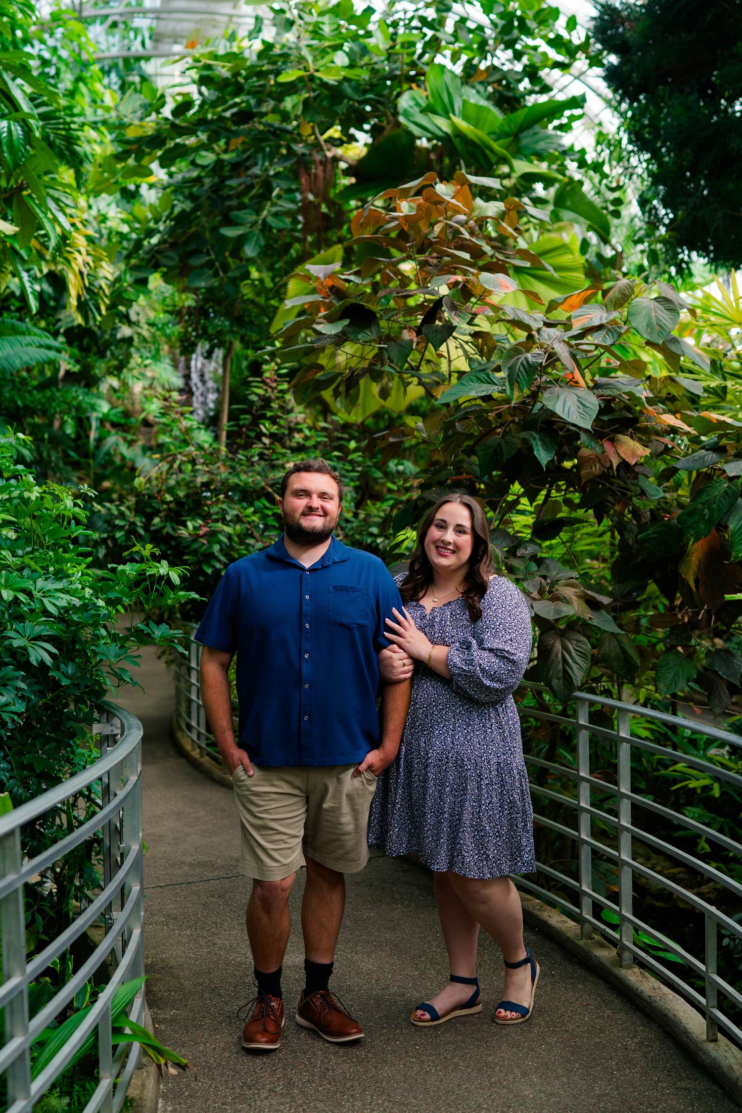 Couple smiling together on a lush botanical garden pathway surrounded by tropical greenery.