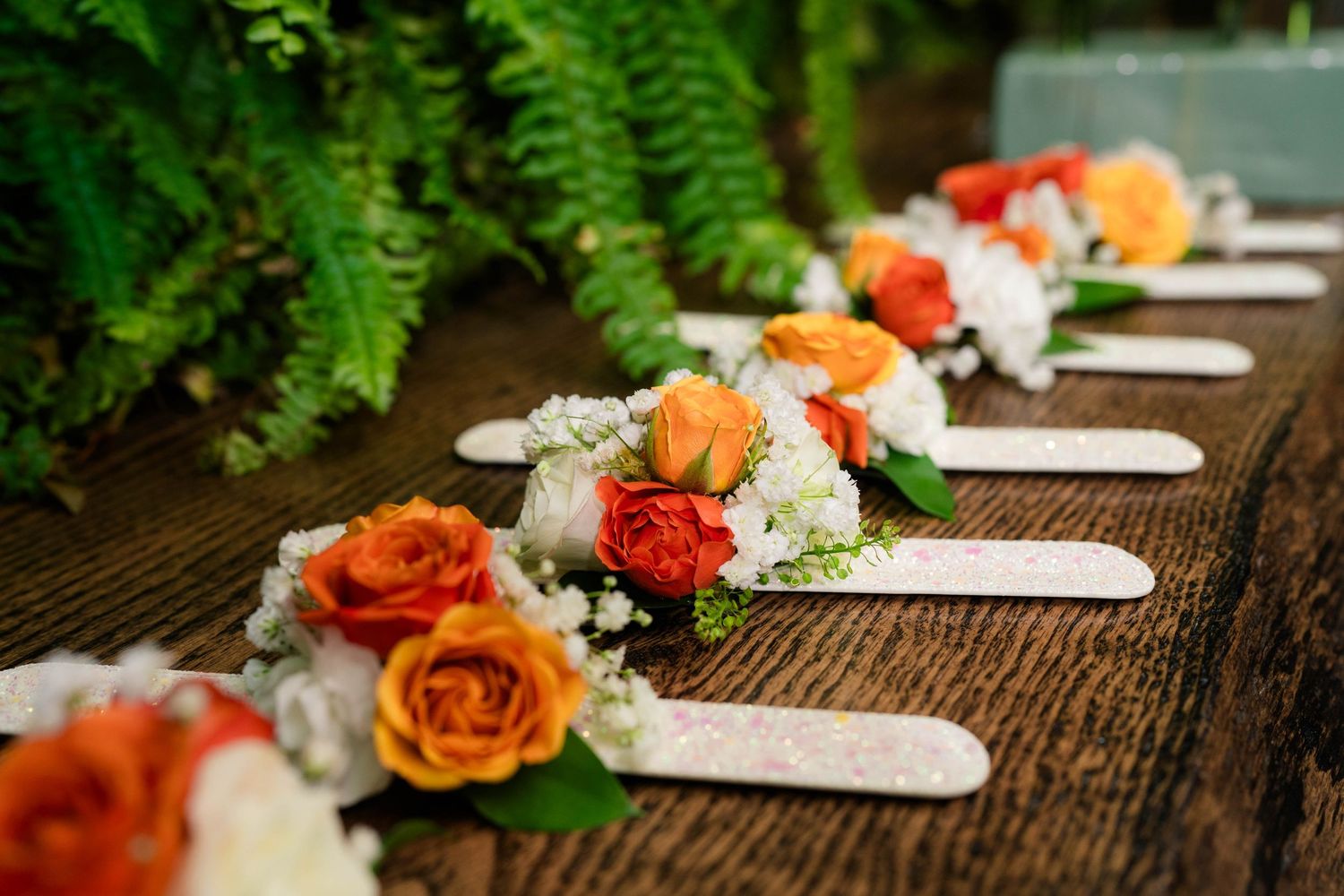Row of orange and white floral corsages with name tags on a rustic wooden table.