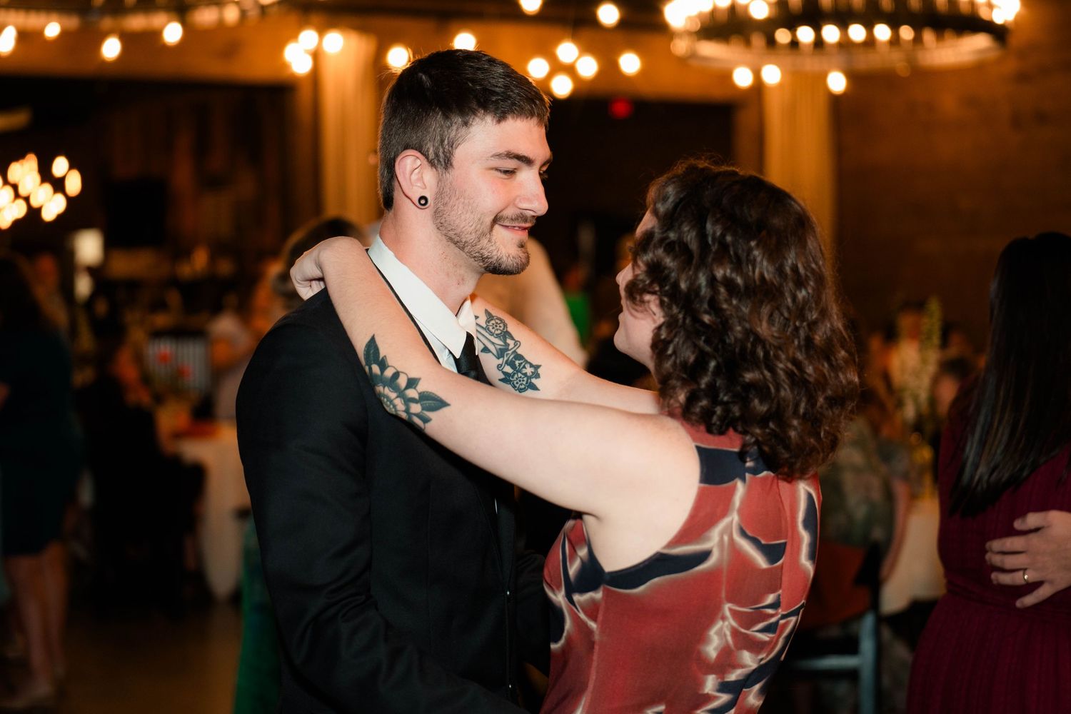 Couple sharing a romantic slow dance at a wedding reception with warm string lights glowing in the background.