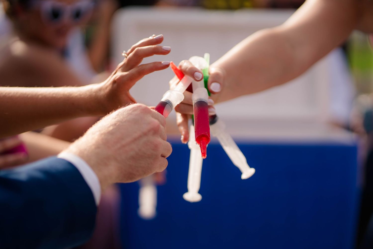 Wedding guests exchange colorful syringes as fun novelty drinks during outdoor wedding celebration.