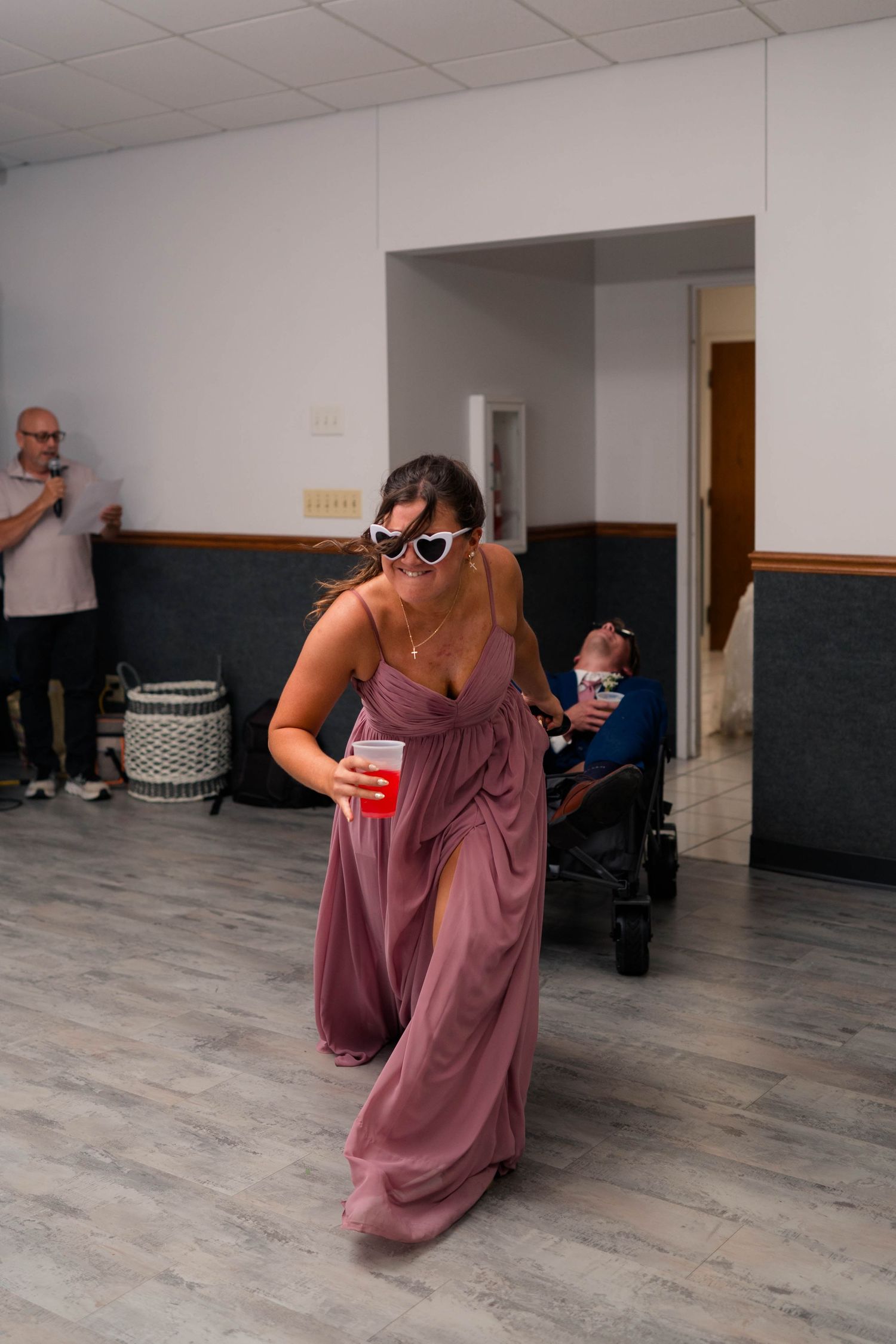 Bridesmaid in mauve dress with white heart sunglasses dancing at wedding reception.