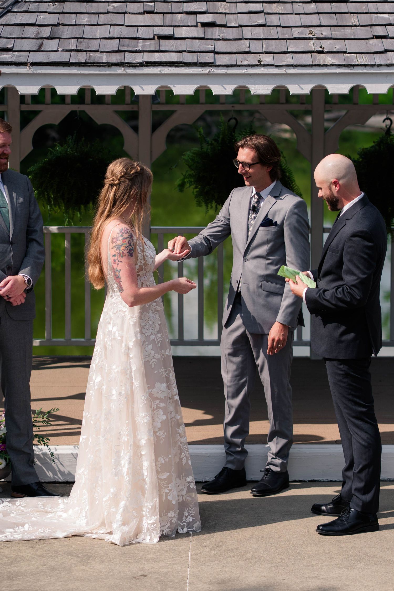 Groom places ring on bride's finger at outdoor gazebo wedding ceremony.