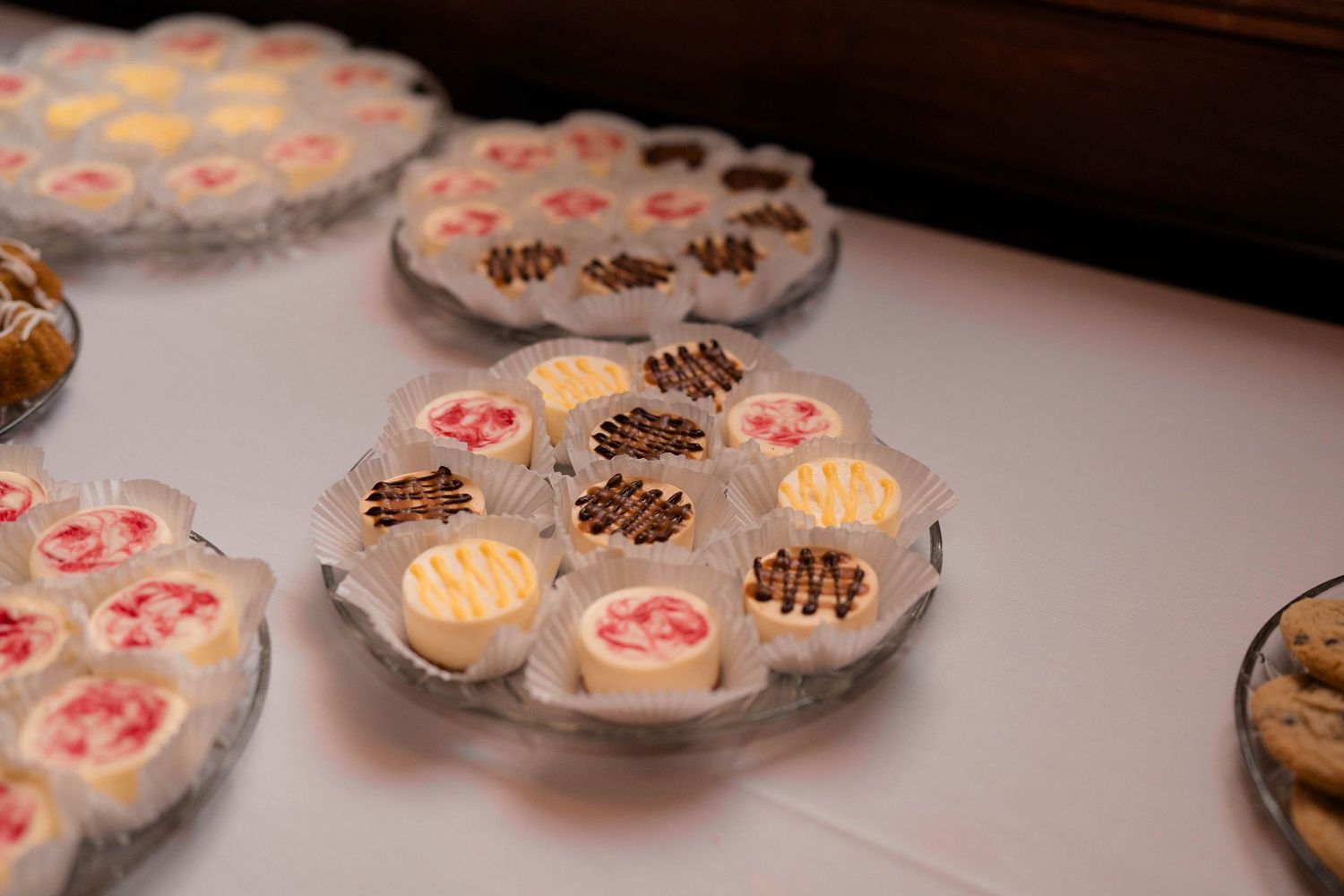 Assorted decorated petit fours and mini cakes displayed on crystal platters at wedding dessert table.