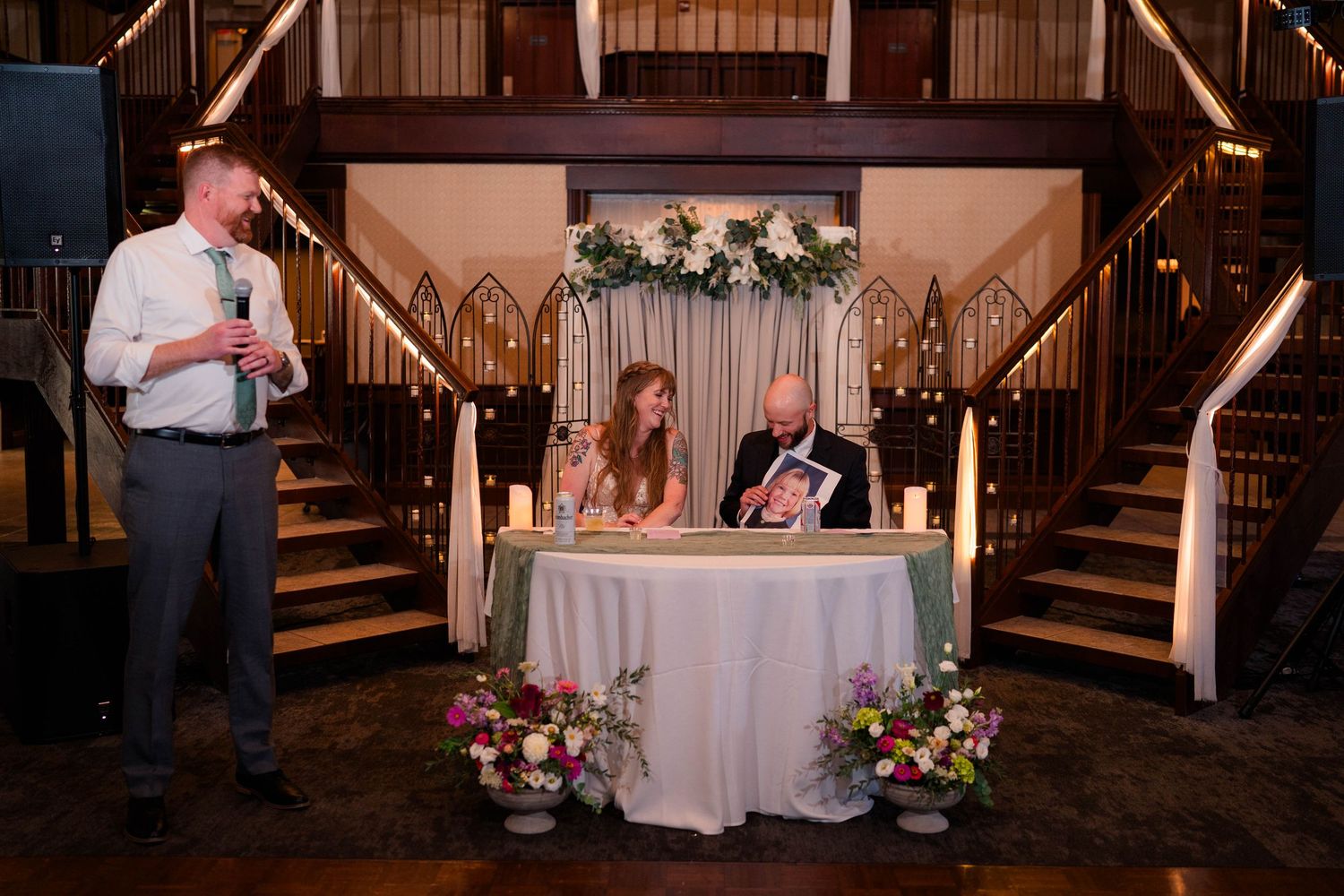 Wedding guest delivers a heartfelt speech at candlelit reception while couple sits at sweetheart table.