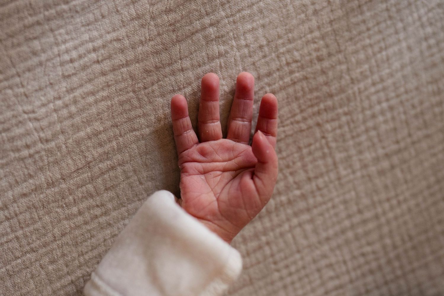 Close-up of a newborn baby's tiny open hand resting on a soft beige textured surface.