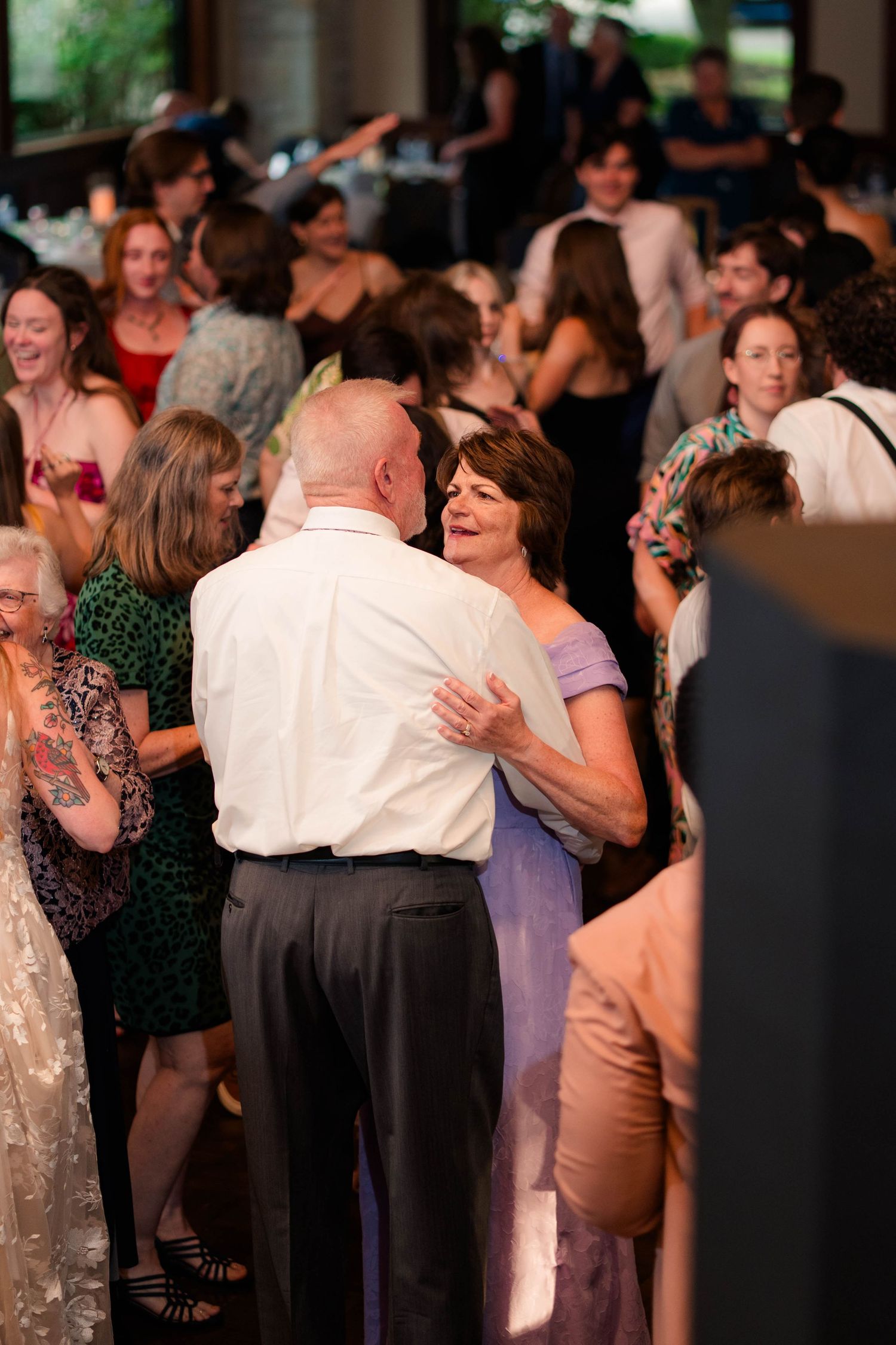 Guests dance joyfully together at a lively wedding reception, with a bald man and woman sharing a dance.