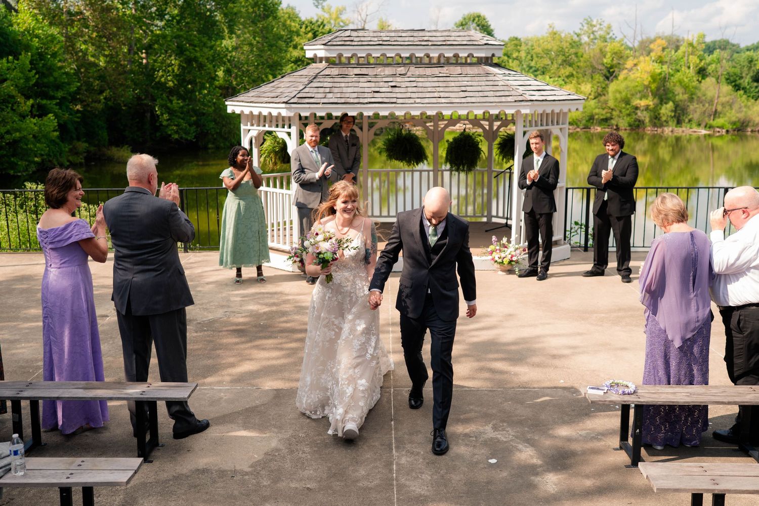Newlyweds recessional walk at outdoor gazebo wedding ceremony by a lake.
