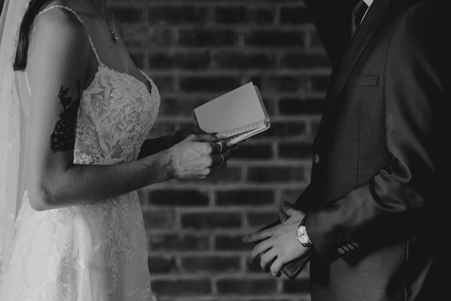 Black and white close-up of bride and groom exchanging vows holding a book at altar.