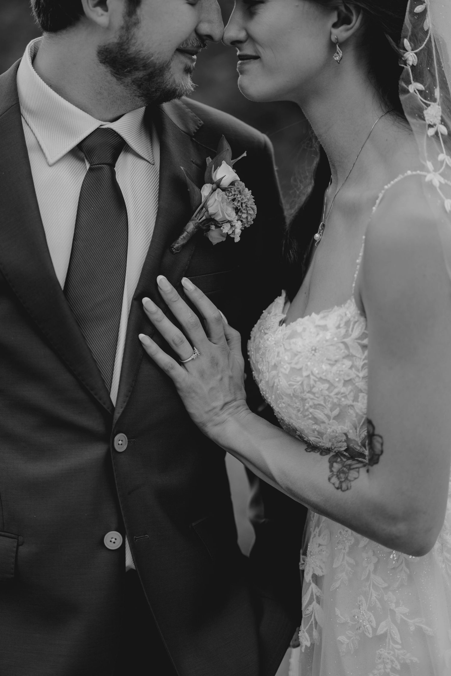 Black and white close-up of bride and groom nearly kissing, bride's hand on groom's chest showing wedding ring.