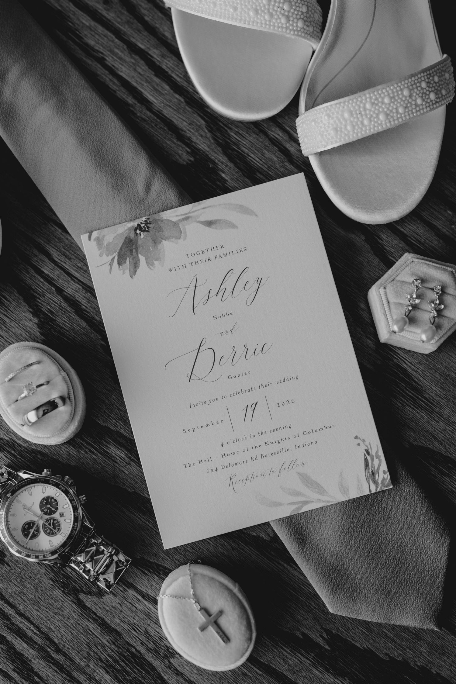 Black and white flat lay of Ashley and Derrie wedding invitation surrounded by bridal accessories.