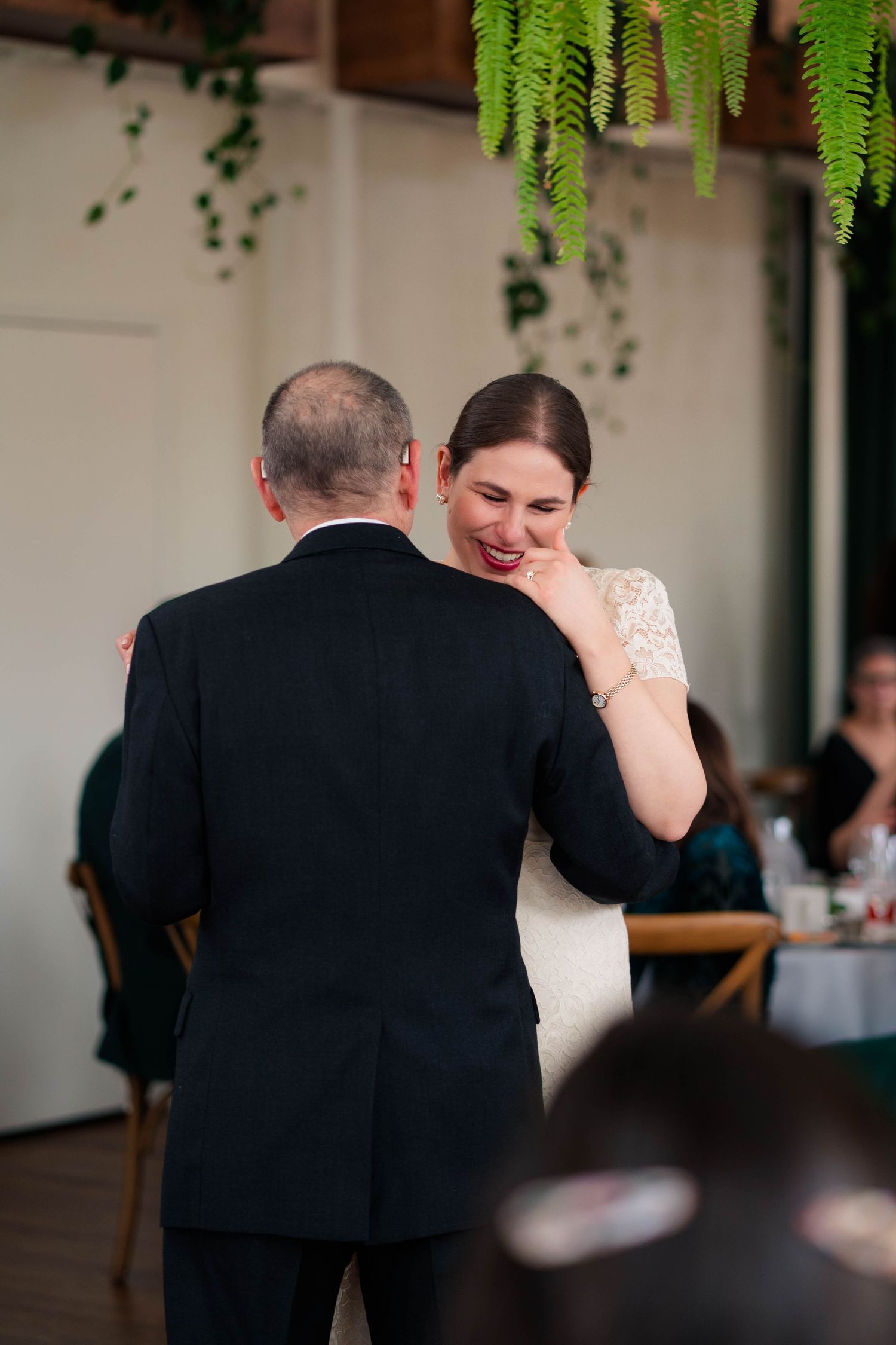 Bride wiping tears while sharing an emotional father-daughter dance at wedding reception.