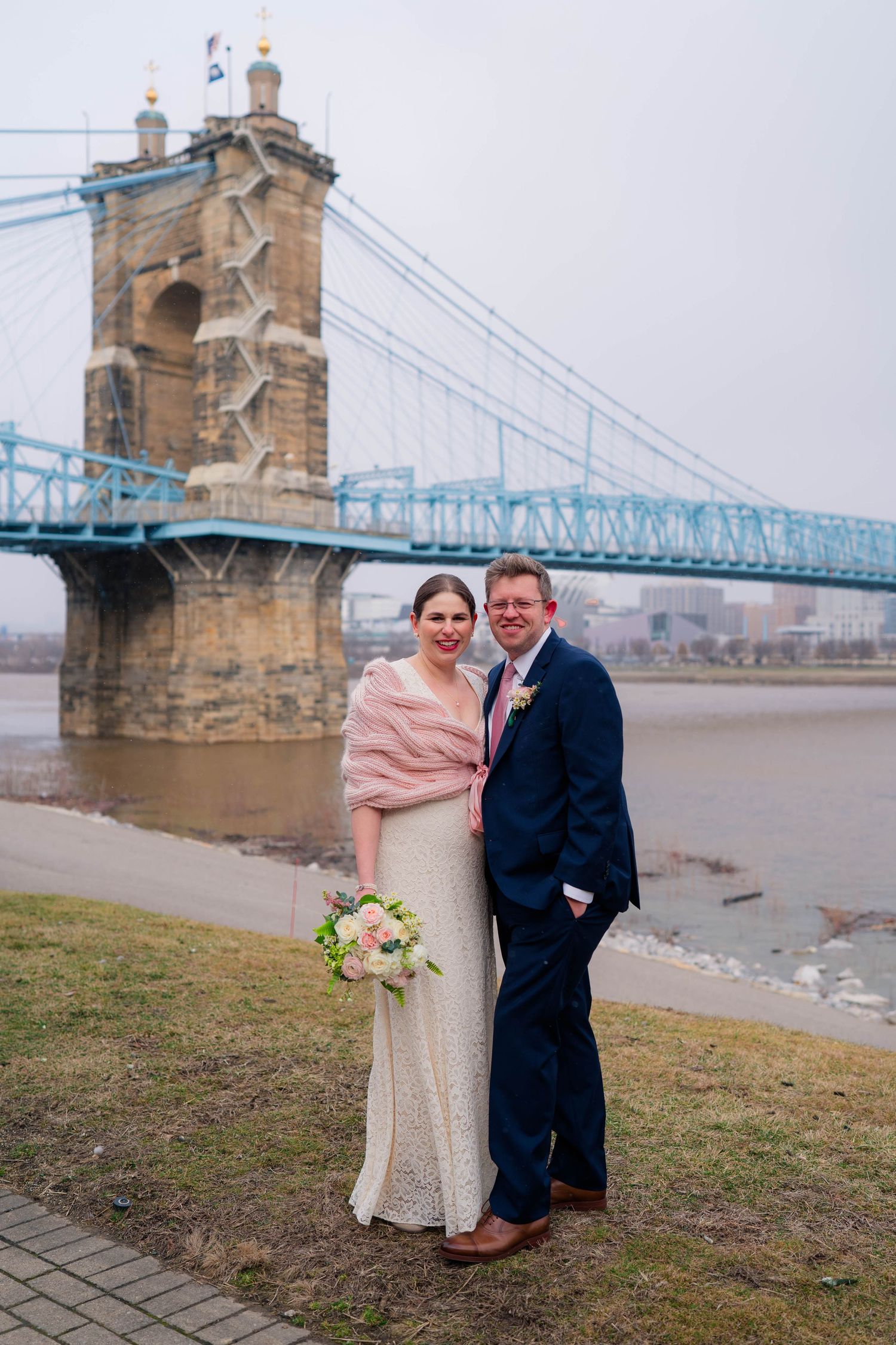 Bride and groom posing before the Roebling Suspension Bridge on their winter wedding day.