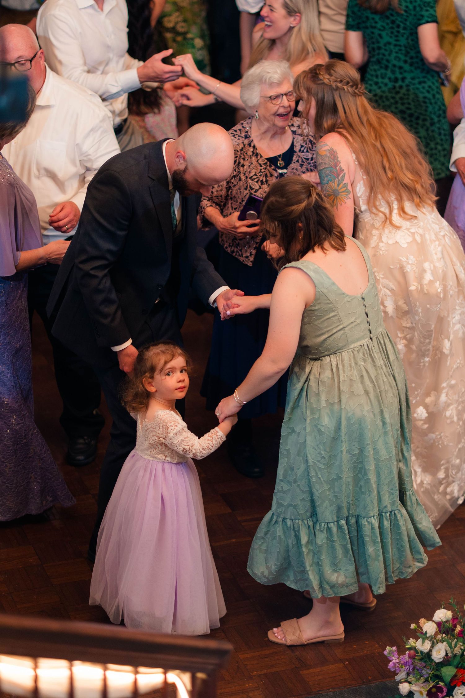 Bald groom dancing with young flower girl in purple tutu at lively wedding reception.