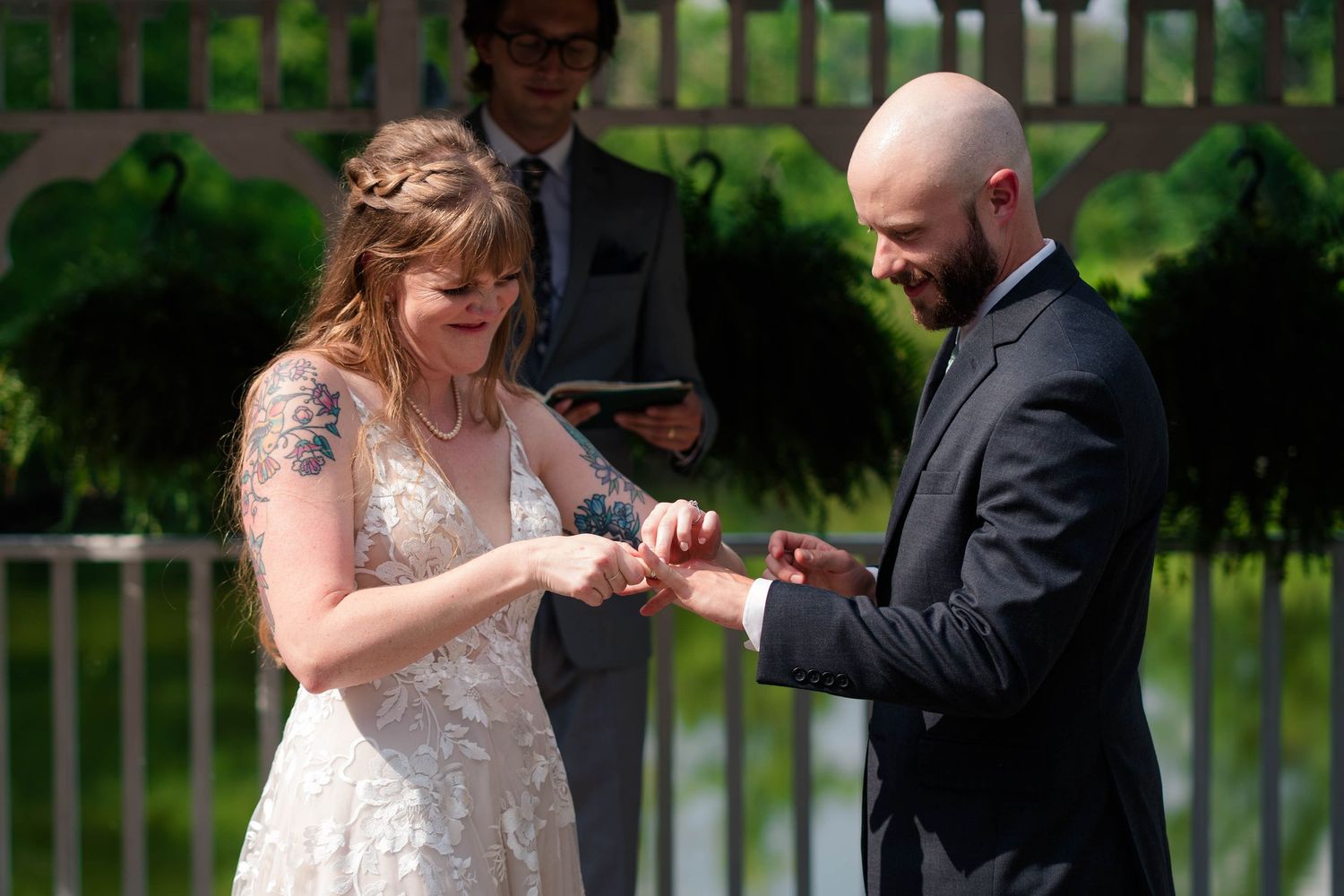 Bride and groom exchanging rings during outdoor wedding ceremony with officiant behind them.