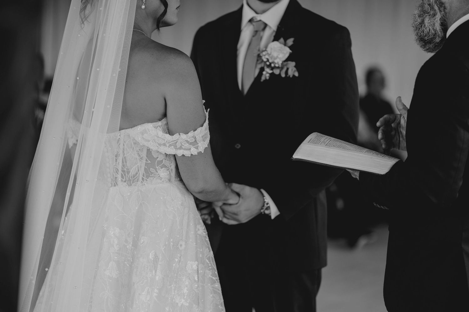 Black and white photo of bride and groom holding hands during wedding ceremony.