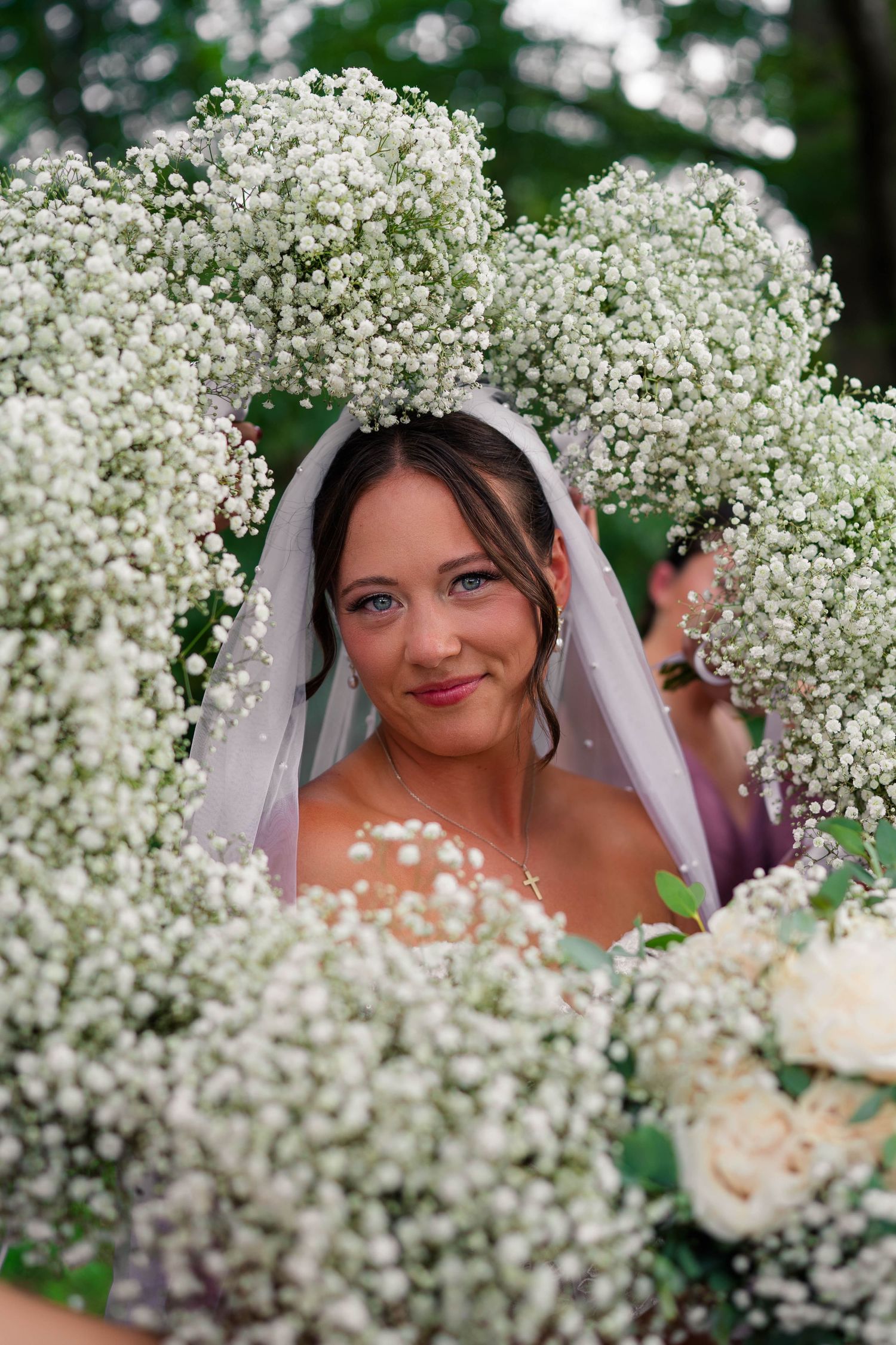 Bride in veil surrounded by large baby's breath bouquets smiling at wedding ceremony.
