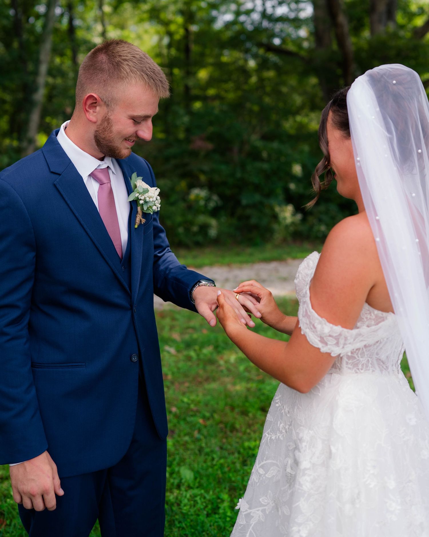 Bride placing wedding ring on groom's finger outdoors during intimate ring exchange ceremony.