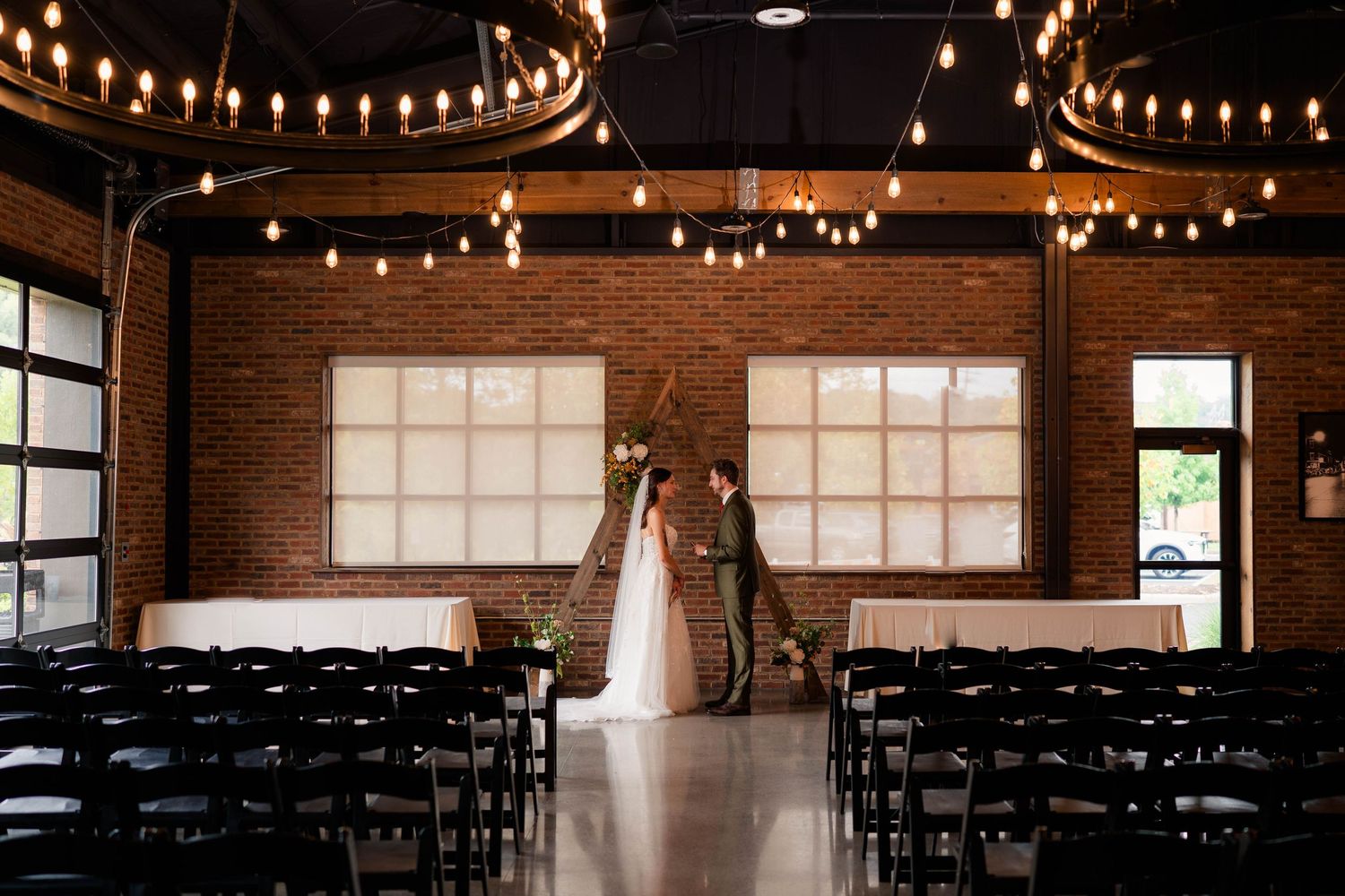Bride and groom standing at rustic brick venue altar with Edison bulb lighting before ceremony.