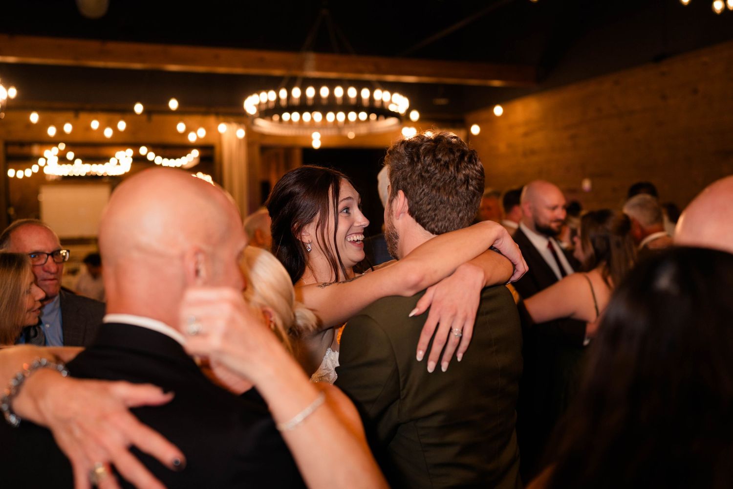 Bride and groom embrace joyfully on crowded dance floor during lively wedding reception celebration.
