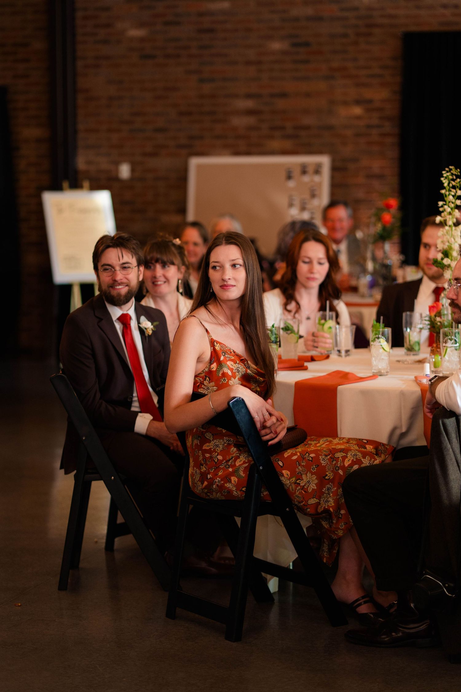 Wedding guests seated at decorated tables during a reception in a brick-walled venue.