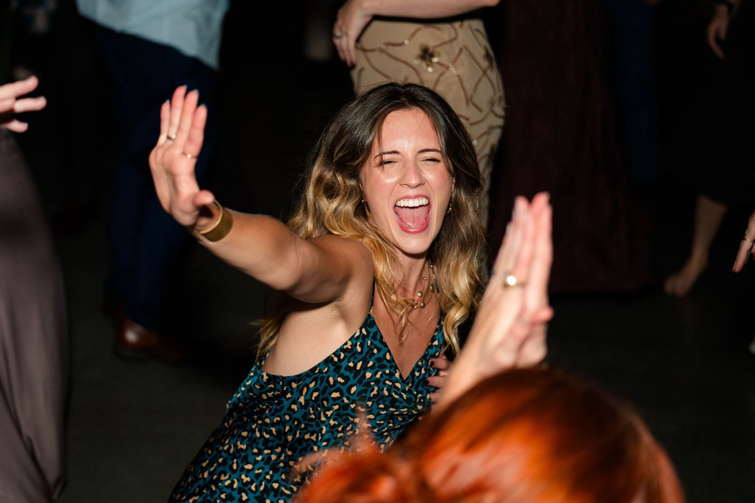 Woman dancing enthusiastically with hands raised at a lively wedding reception celebration.