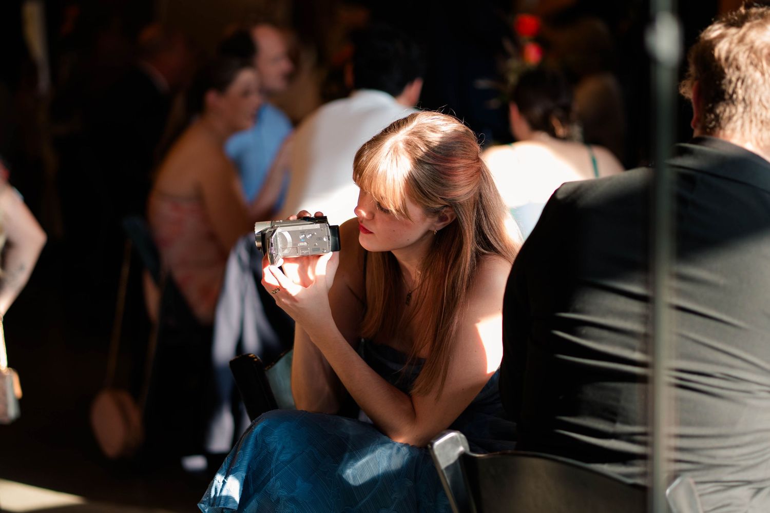 Female wedding guest captures memories using a handheld video camera during reception celebration.