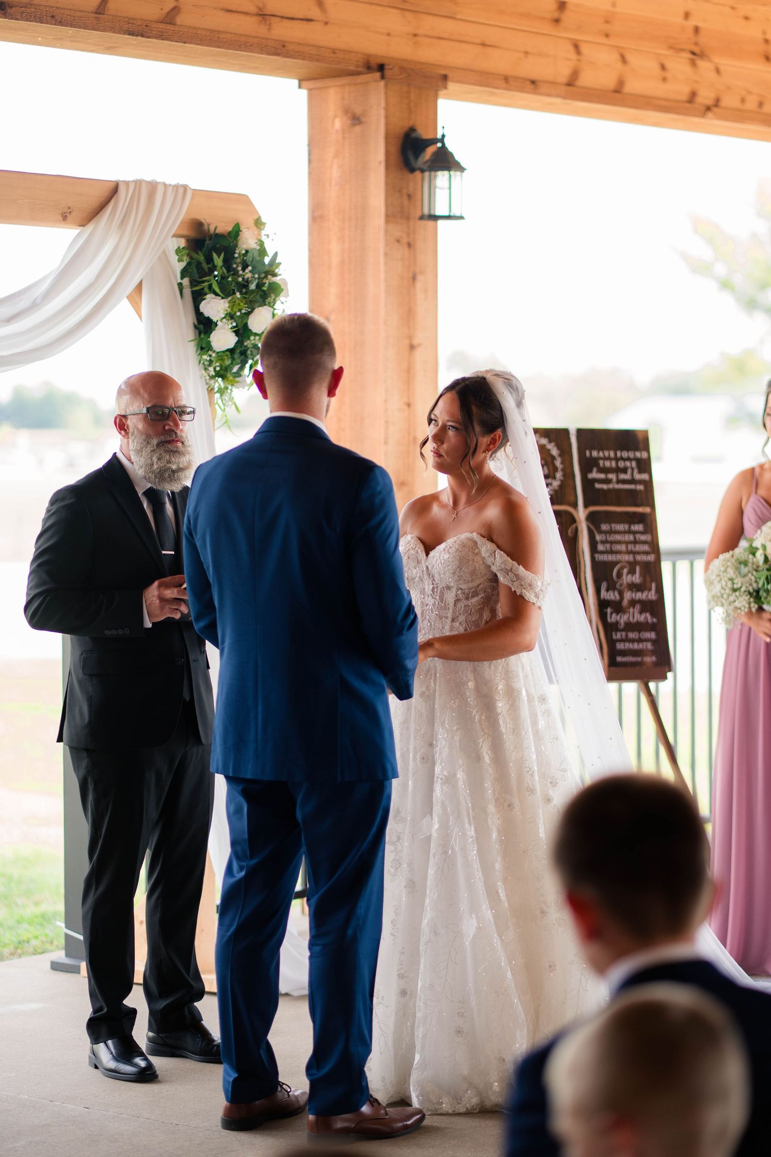 Bride and groom stand at altar with officiant during outdoor covered wedding ceremony.