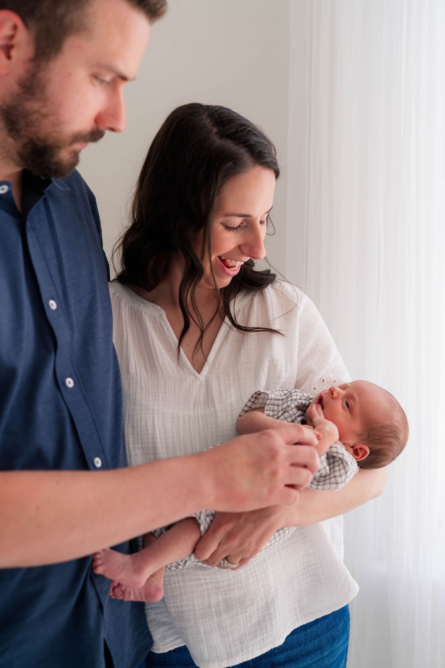 Happy new parents smile at their newborn baby during an intimate indoor newborn photography session.