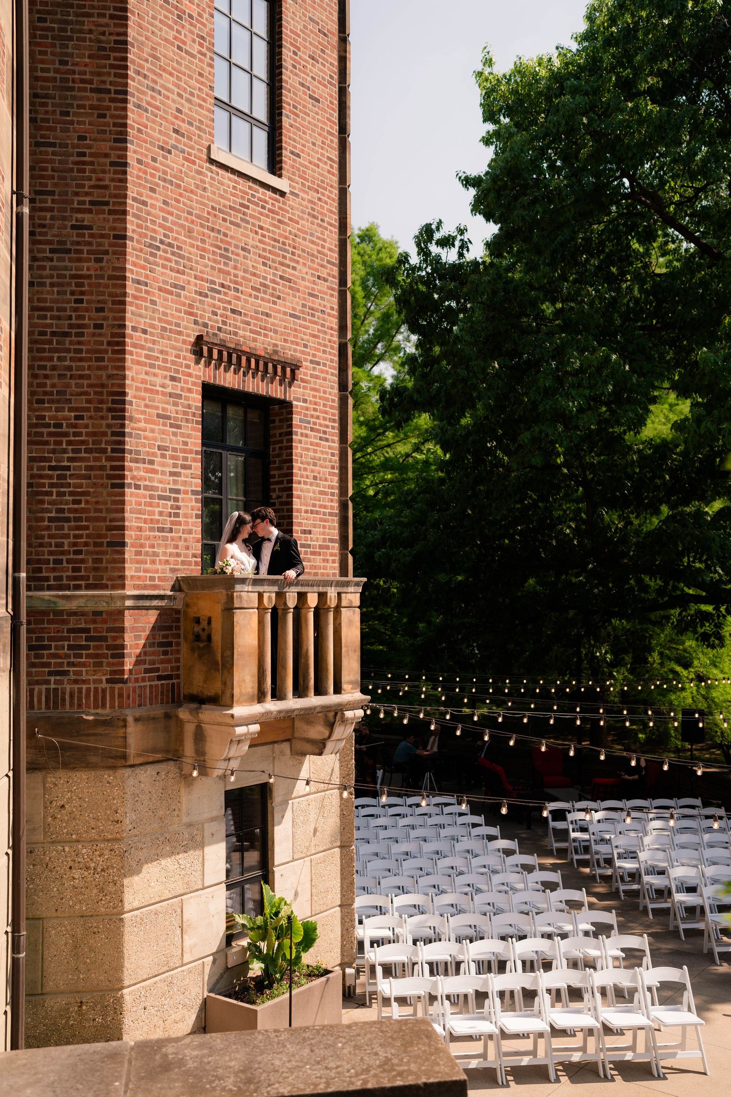 Bride and groom share a romantic moment on a balcony above rows of white ceremony chairs.