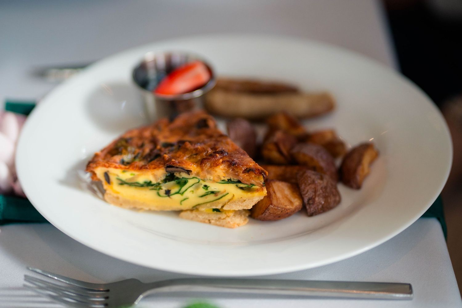 Savory spinach omelette served with roasted potatoes, sausage, and fresh strawberry on a white plate.