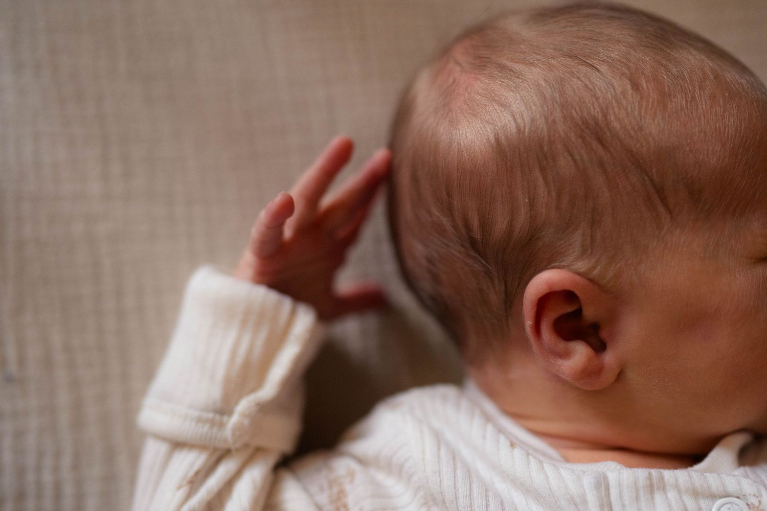 Close-up of a newborn baby's head and tiny hand wearing a white knit outfit.